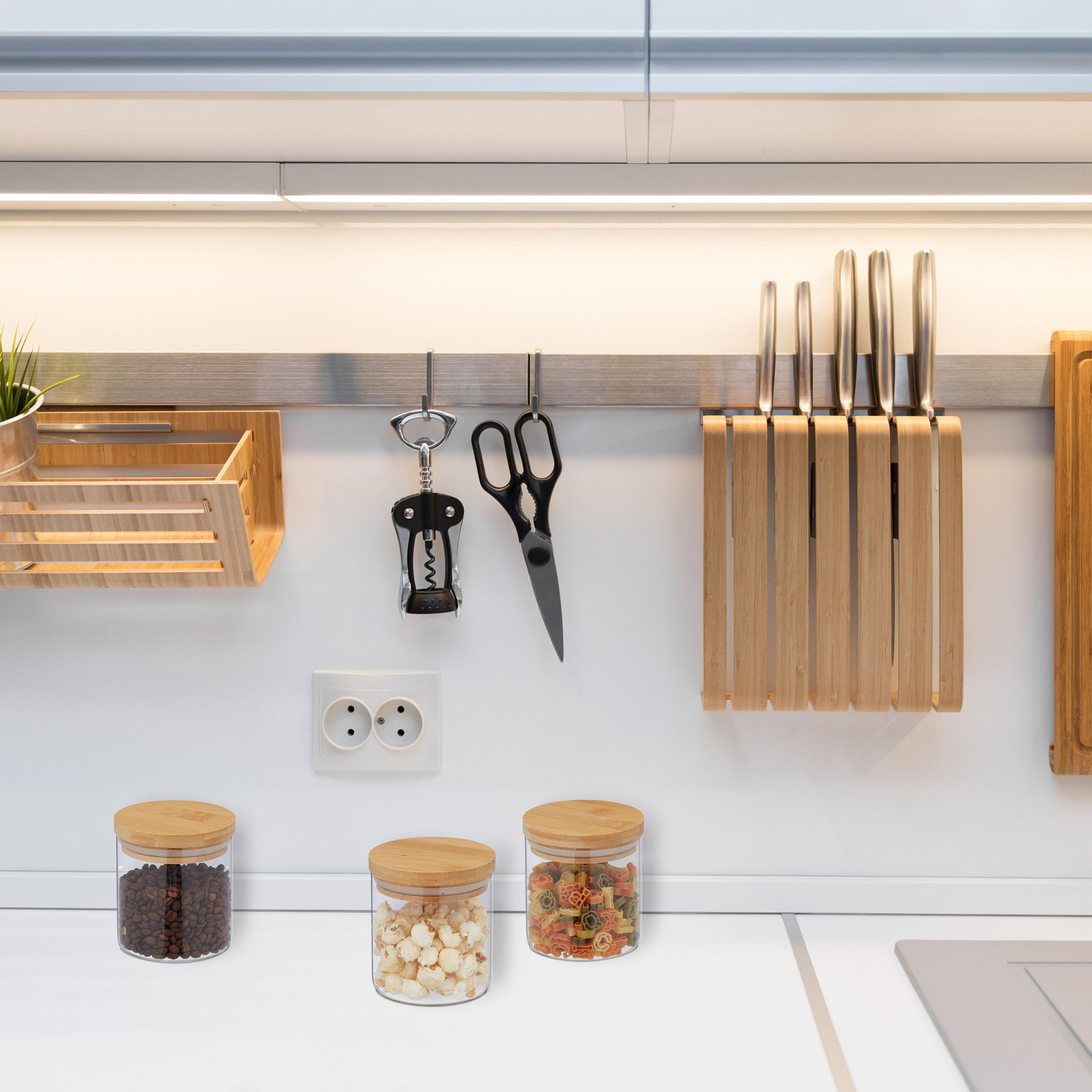 Moderne Küchenwand mit Hängeschiene, Holzmessern, Utensilien und Gläsern mit Lebensmitteln auf der Arbeitsplatte.
