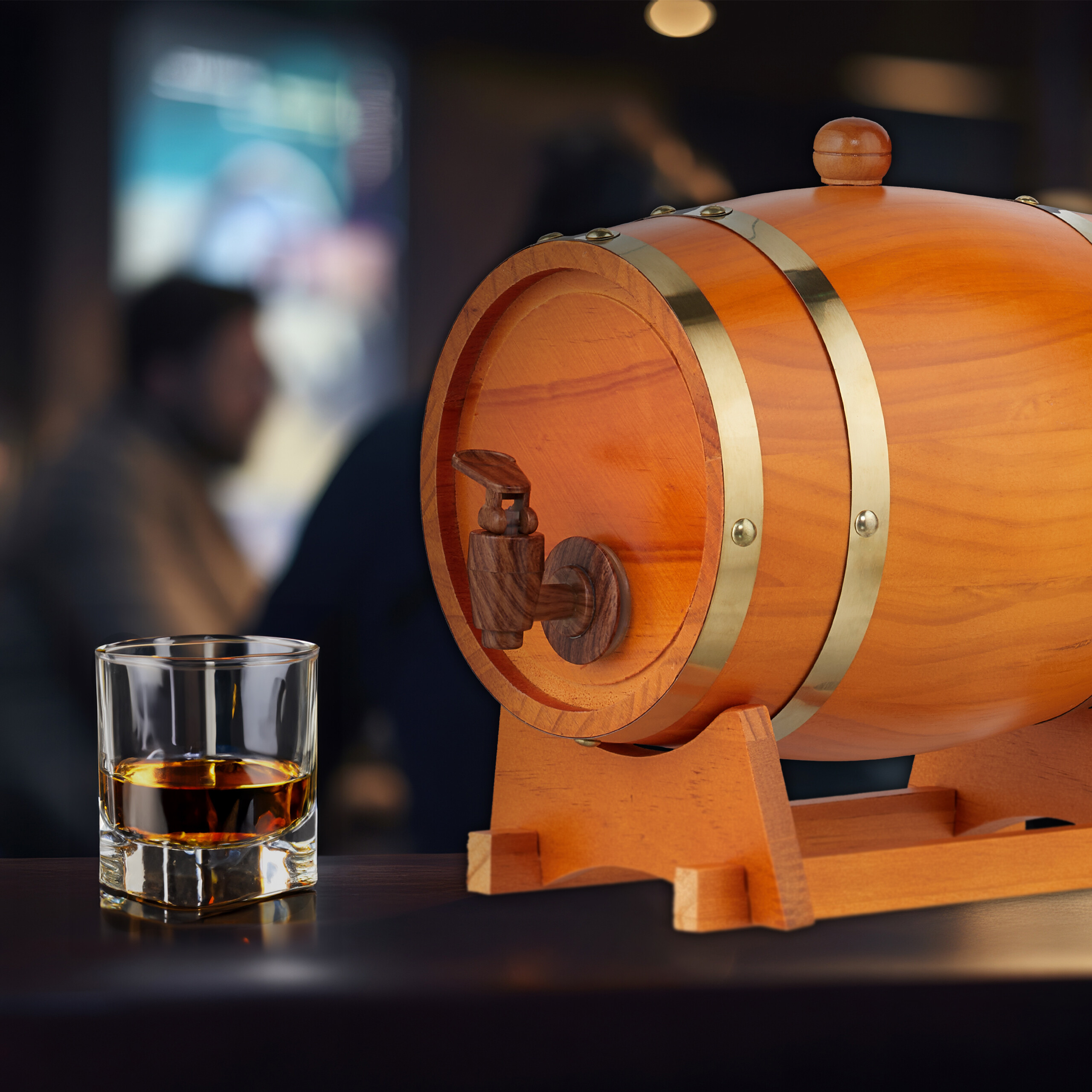 Ein Holzfass mit Hahn und ein Glas Whisky auf einer Theke vor verschwommenem Hintergrund.