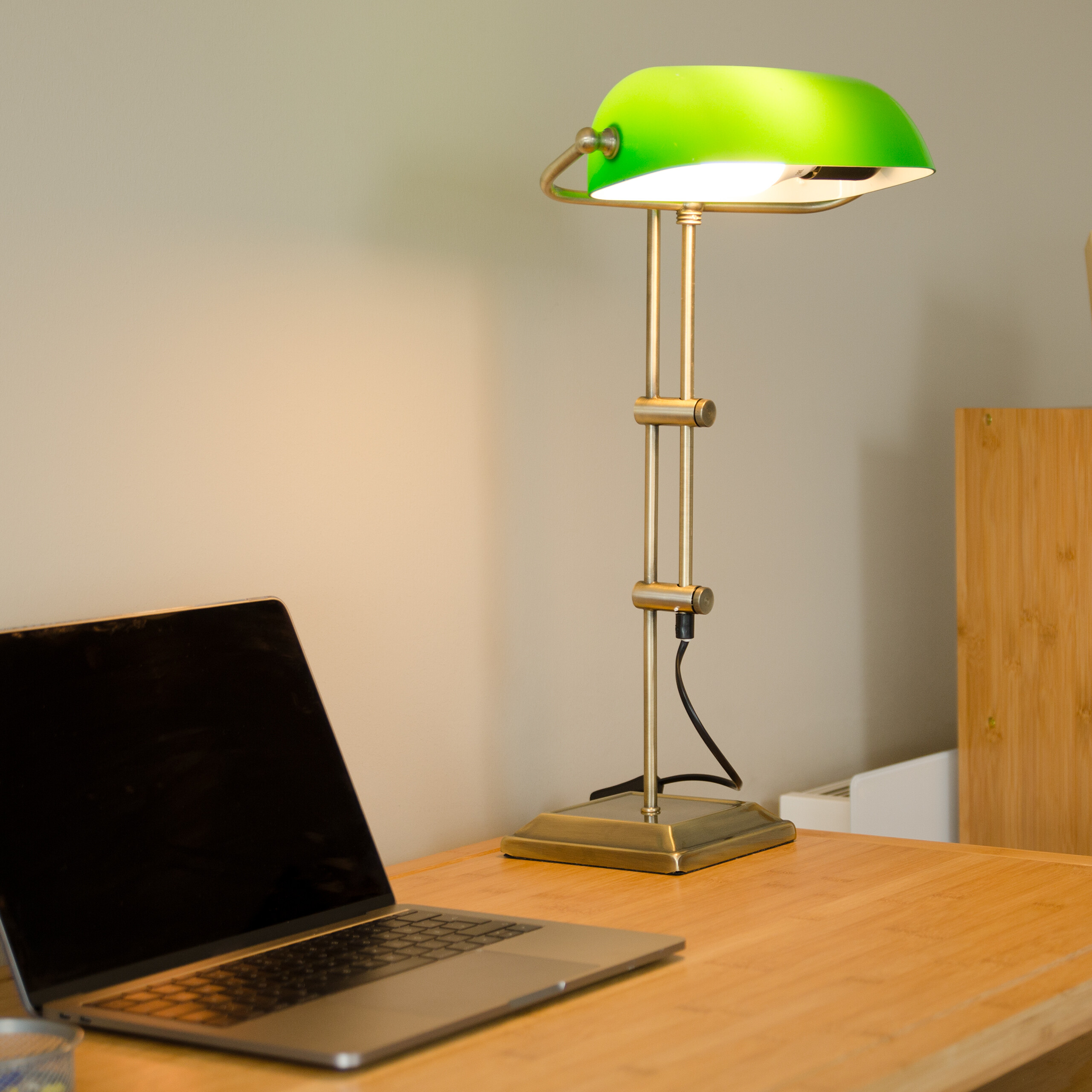 Eine grüne Schreibtischlampe und ein Laptop stehen auf einem Holztisch.