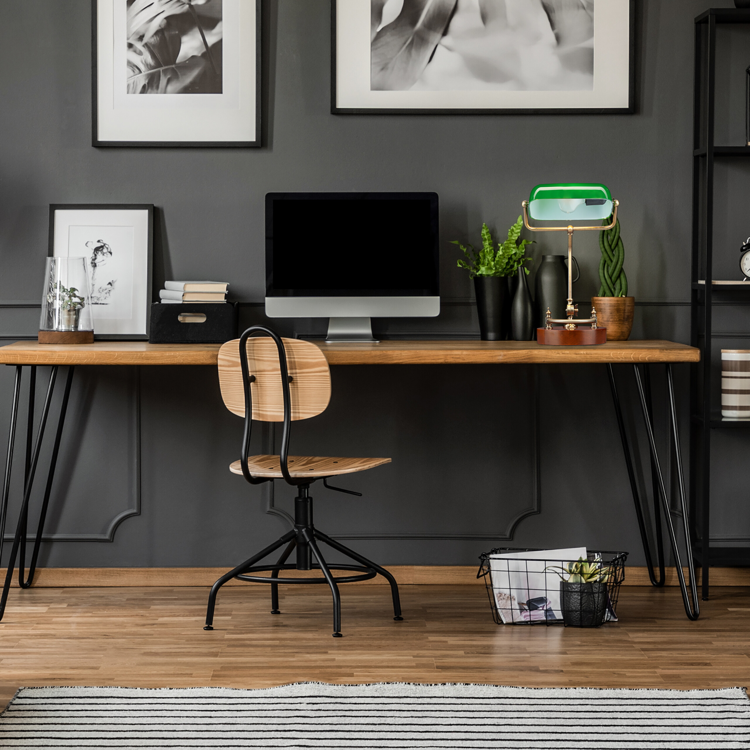 Moderne Schreibtisch-Einrichtung mit Holzplatte, Computer, Stuhl und Pflanzen vor einer dunklen Wand.