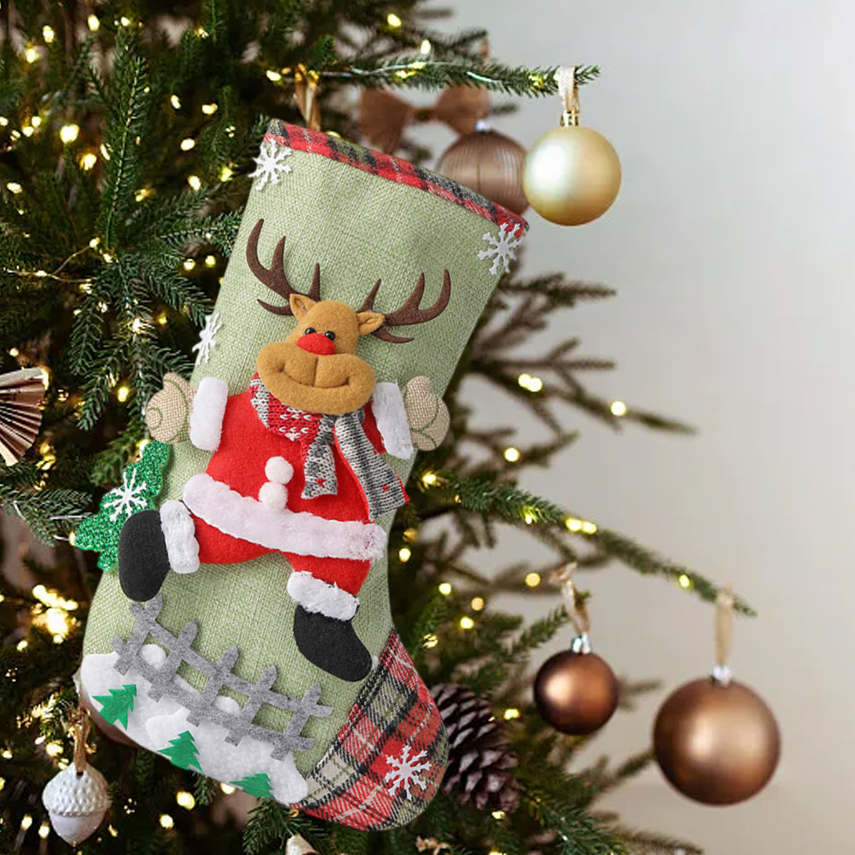 Grüner Weihnachtsstrumpf mit Plüschrentier hängt an einem Weihnachtsbaum mit Lichtern.