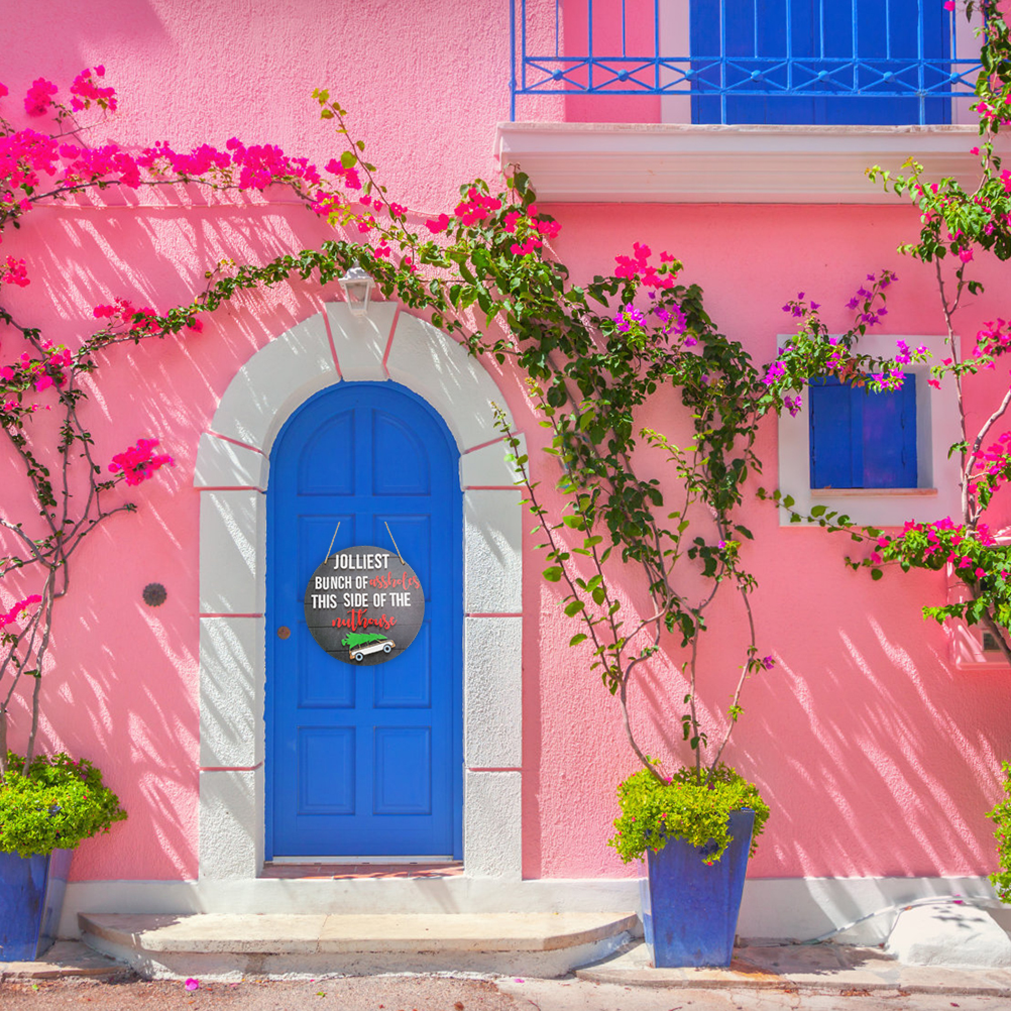Eine leuchtend rosa Wand mit blauer Tür und Fenstern, geschmückt mit grünen Kletterpflanzen und pinken Blüten.