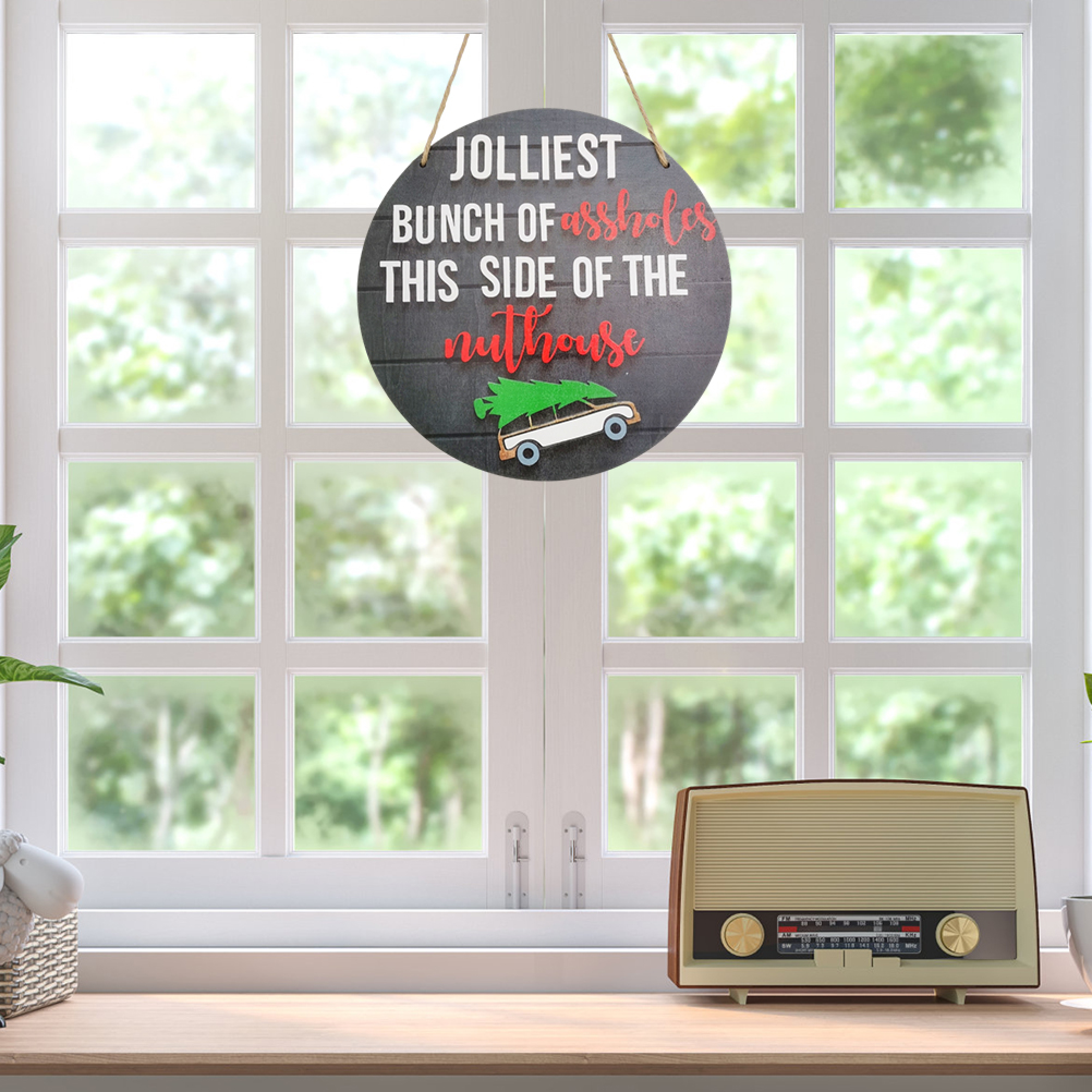 Ein rundes Holzschild mit Spruch hängt vor einem Fenster, daneben ein Retroradio.