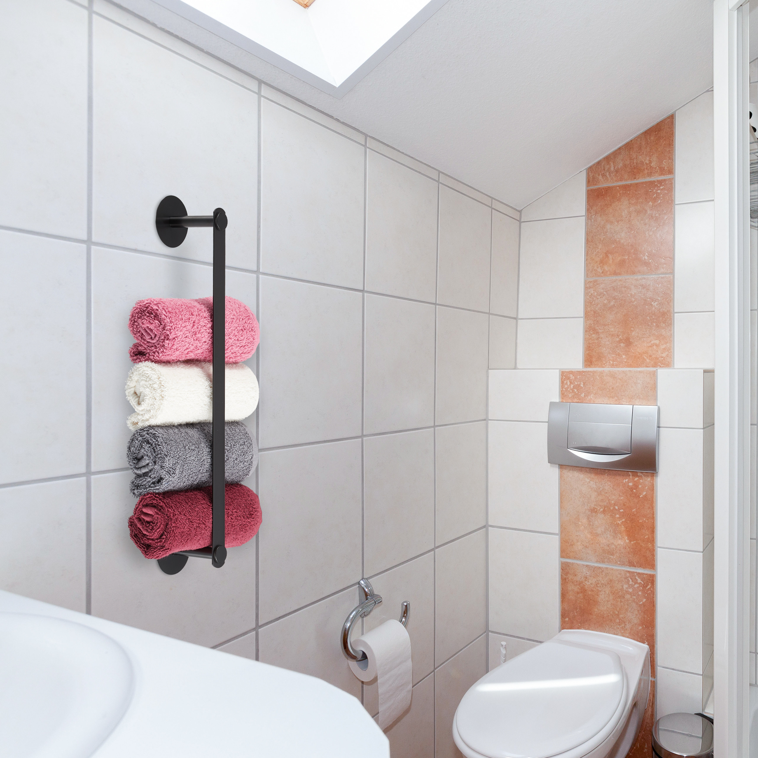 Moderne Badezimmerwand mit Fliesen, einem schwarzen Handtuchhalter mit vier bunten Handtuchrollen, Toilette und Waschbecken.