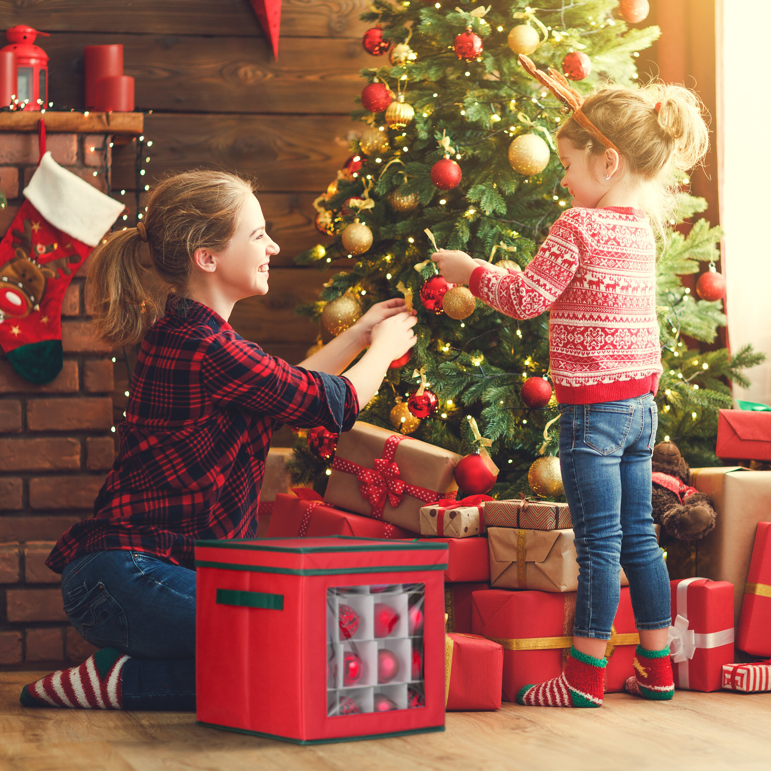 Eine Mutter und Tochter schmücken drinnen einen Weihnachtsbaum, umgeben von Geschenken und Lichtern.
