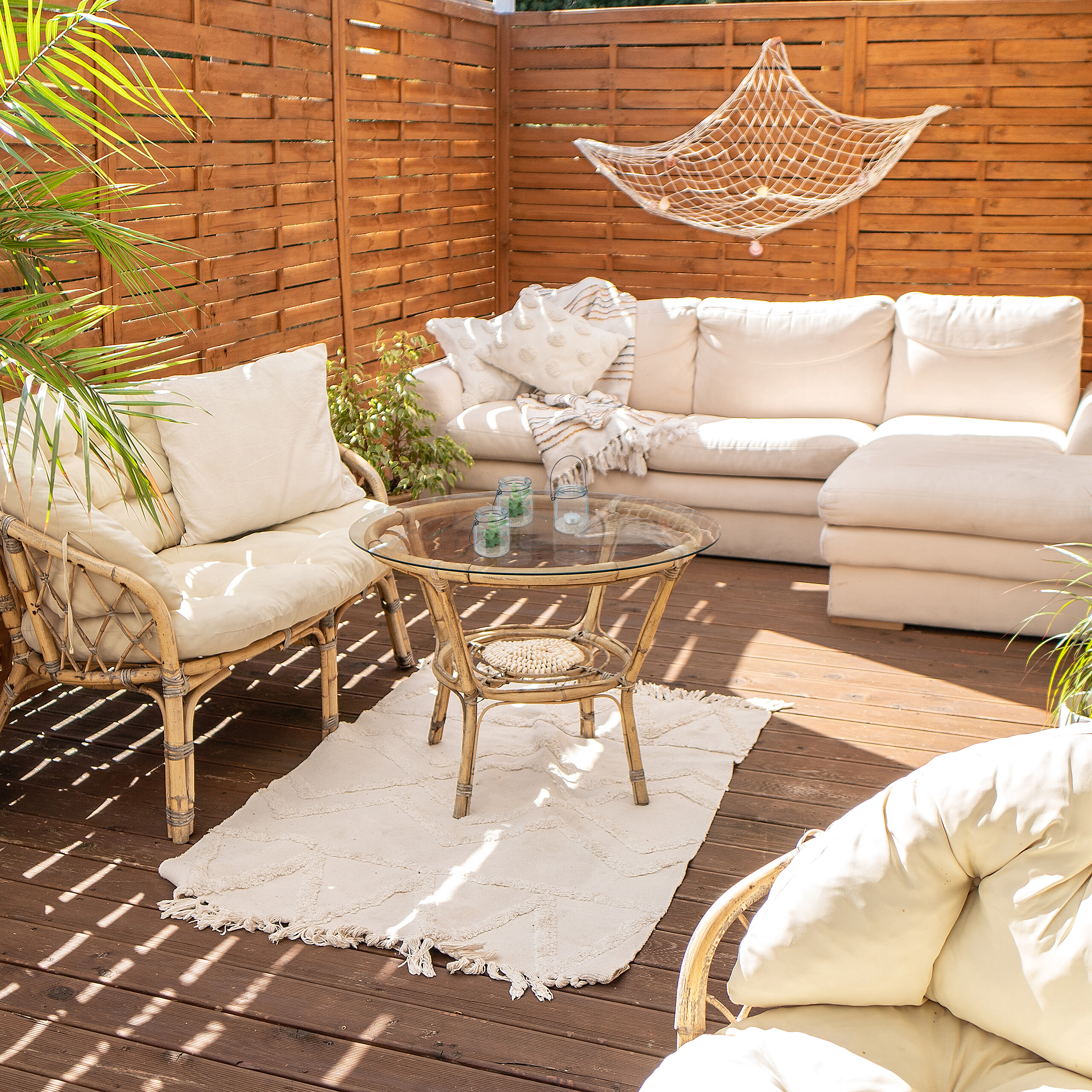 Sonnige Holzterrasse mit weißem Ecksofa, Korbstühlen, Glastisch, weißem Teppich und Hängedekor.