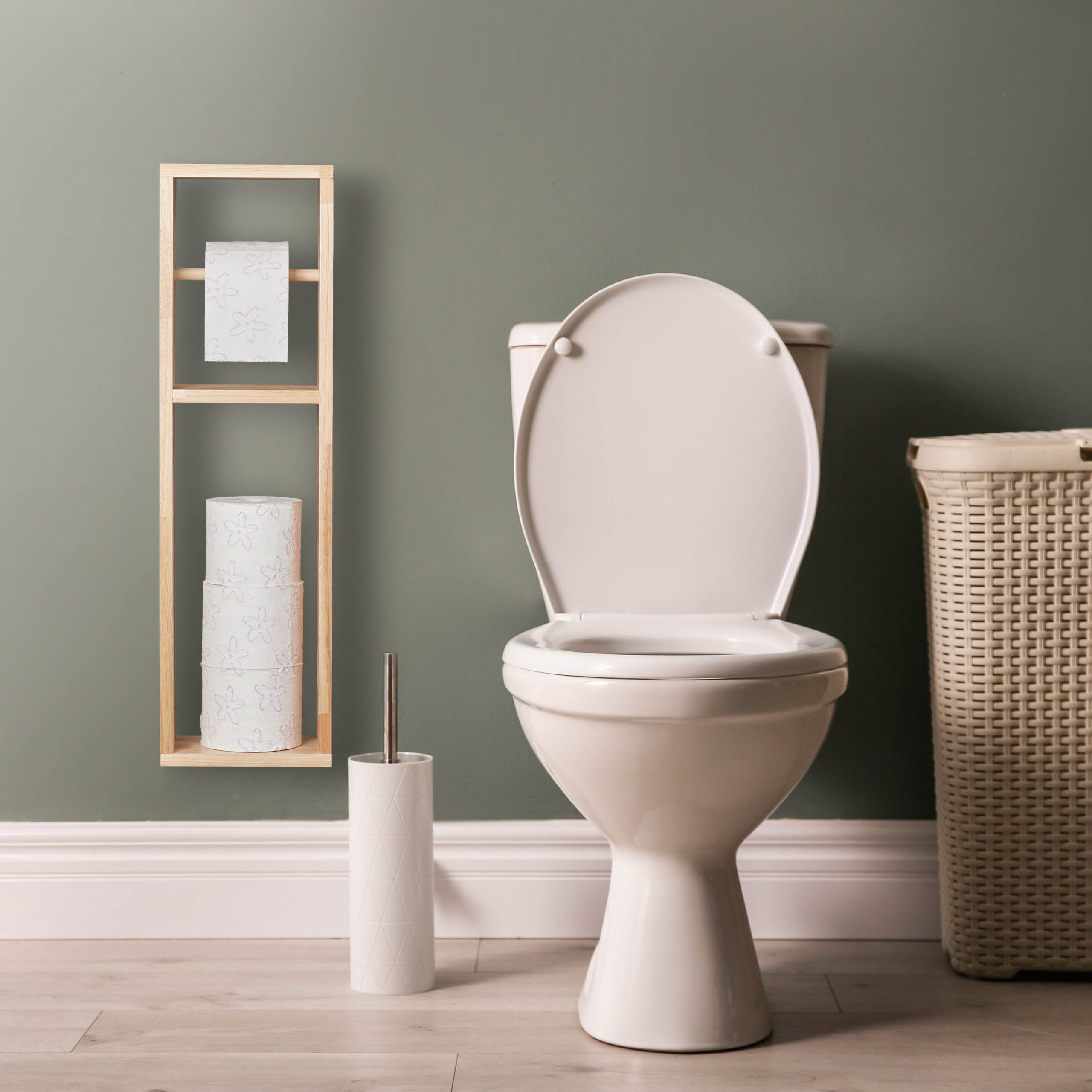 Eine weiße Toilette steht in einem Raum mit grünen Wänden, einem Holzwandregal, einer Klobürste und einem Wäschekorb.