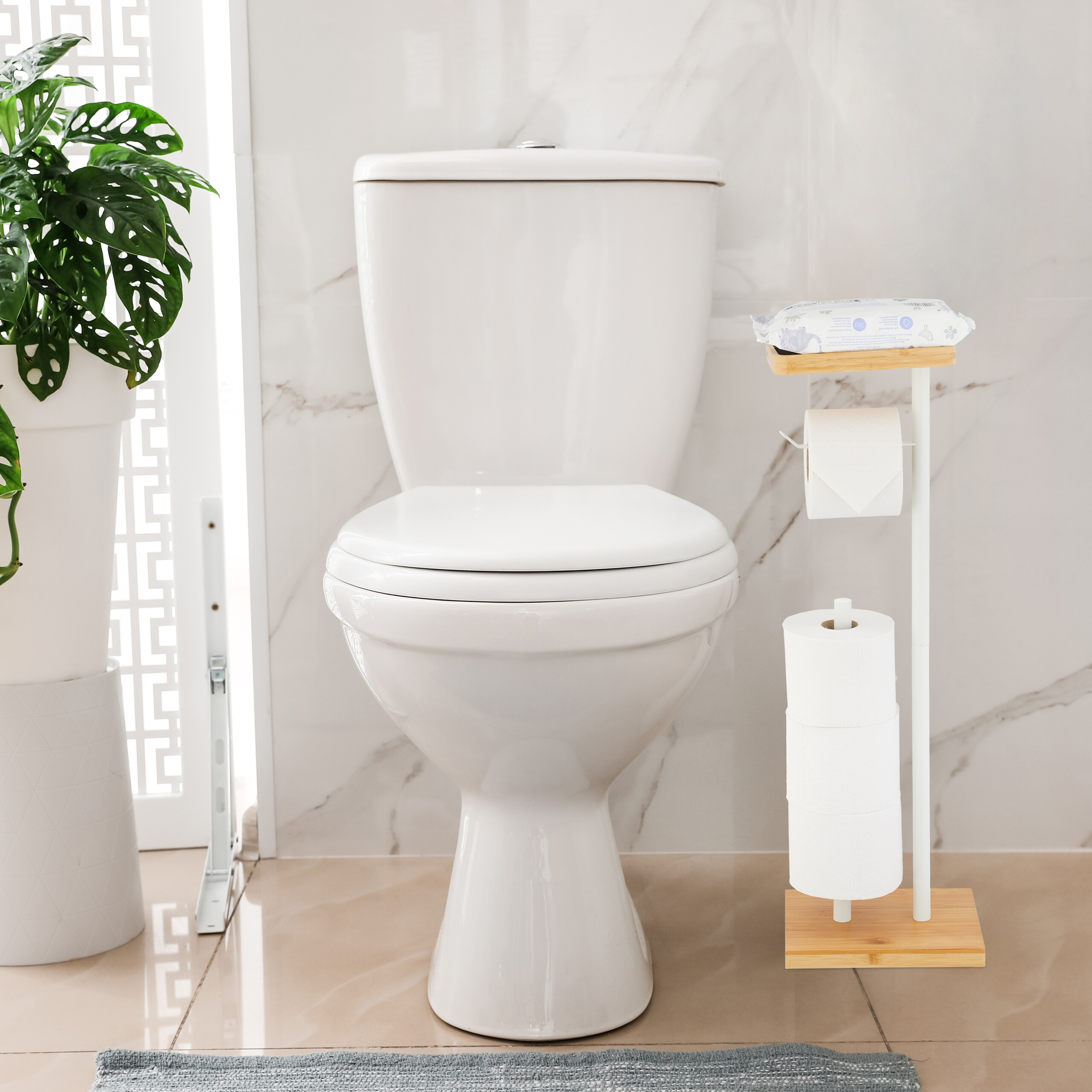 Eine weiße Toilette steht in einem Badezimmer mit Marmorwänden, daneben ein Toilettenpapierhalter und eine grüne Pflanze.