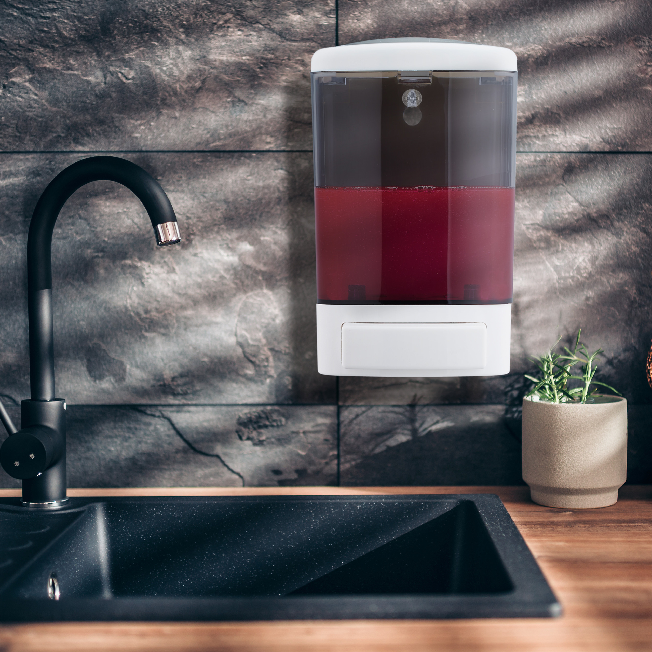 Wandseifenspender mit roter Seife, schwarzes Spülbecken und Wasserhahn vor einer dunklen Fliesenwand.