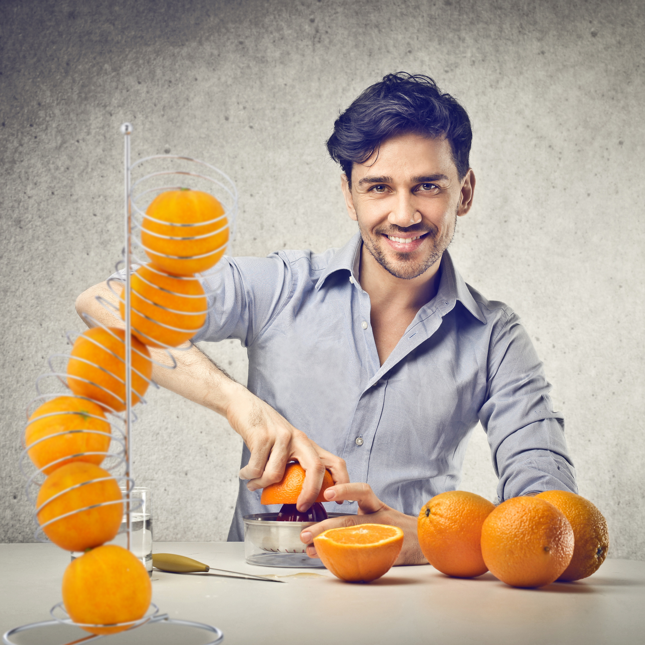 Ein lächelnder Mann in blauem Hemd presst Orangen mit einer Zitruspresse an einem Tisch mit Orangen.