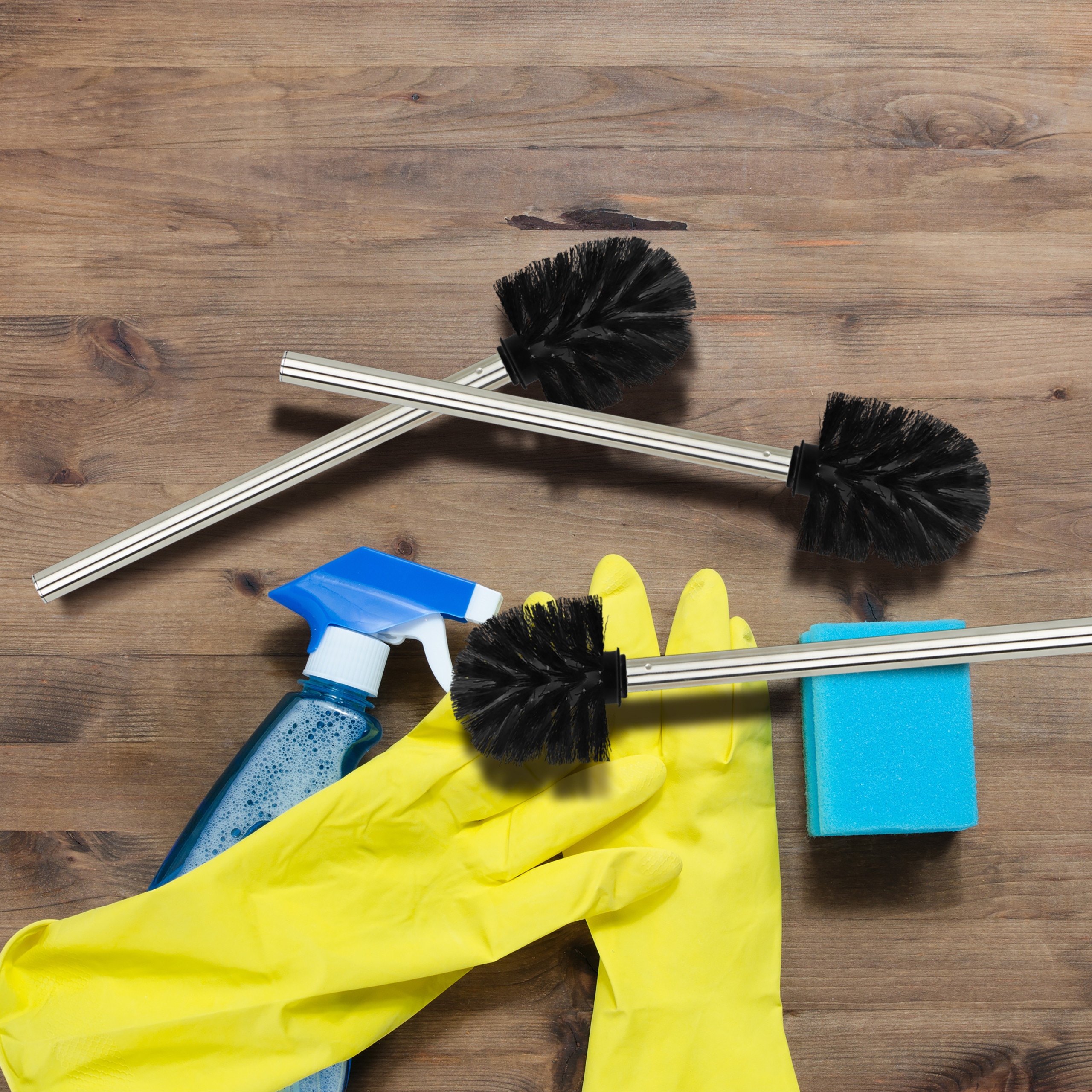 Reinigungswerkzeuge auf Holz: Toilettenbürsten, gelbe Handschuhe, blauer Sprüher und Schwamm.