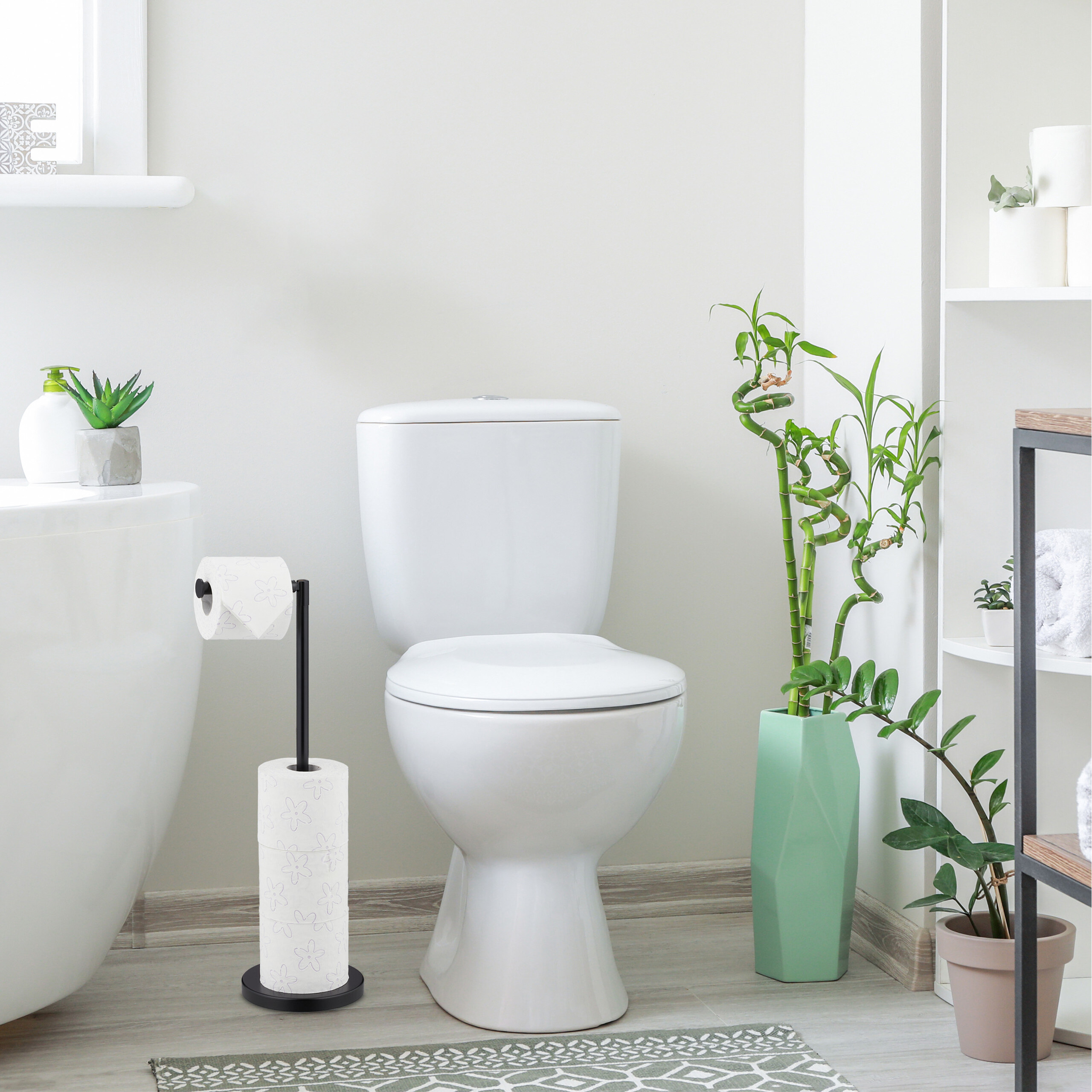 Ein modernes Badezimmer mit weißem WC, schwarzem Toilettenpapierhalter, grünen Pflanzen und Regalen.
