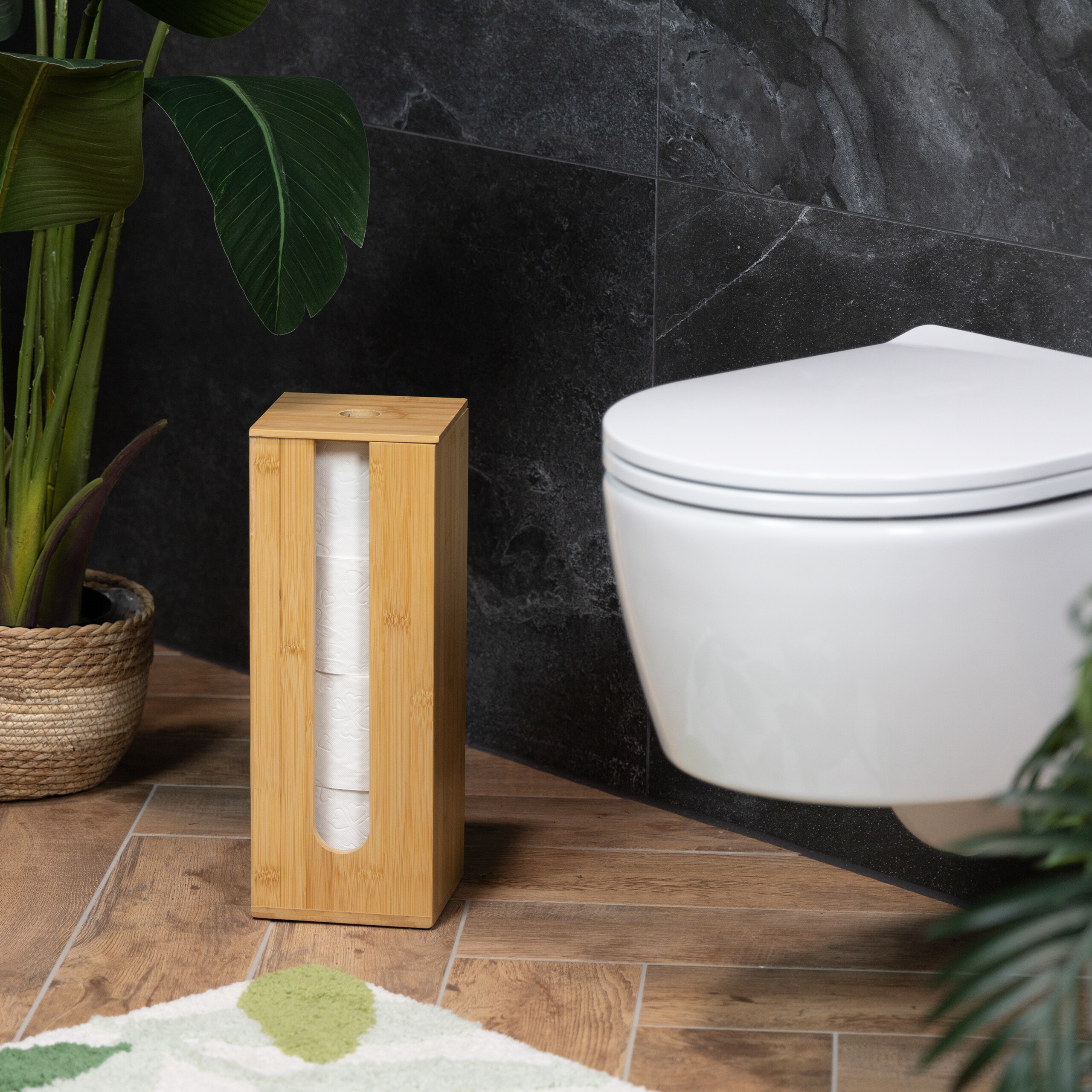 Ein Toilettenpapierhalter aus Holz mit drei Rollen steht auf Holzfliesen neben einer Toilette und einer Pflanze.