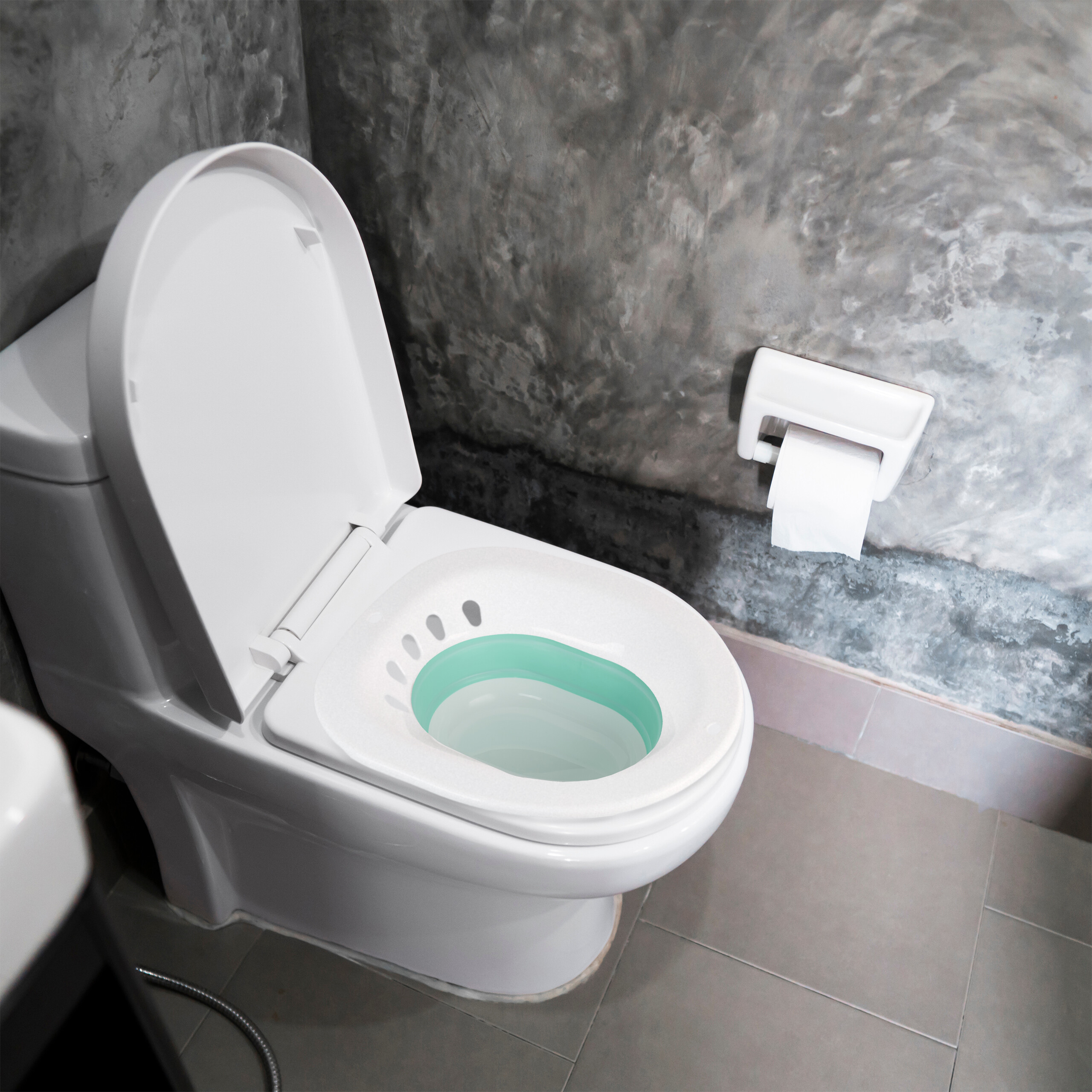 Eine weiße Toilette mit grünem Sitzaufsatz in einem Raum mit grauen Wänden und einem Toilettenpapierhalter.