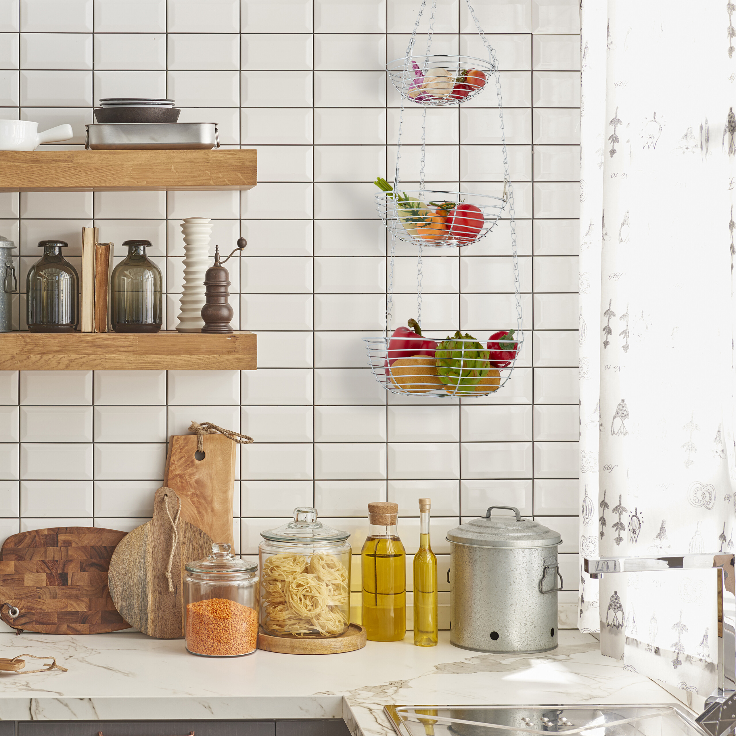 Eine Küche mit Holzböden, hängenden Obstkörben, Gläsern, Schneidebrettern und weißen Fliesen an der Wand.