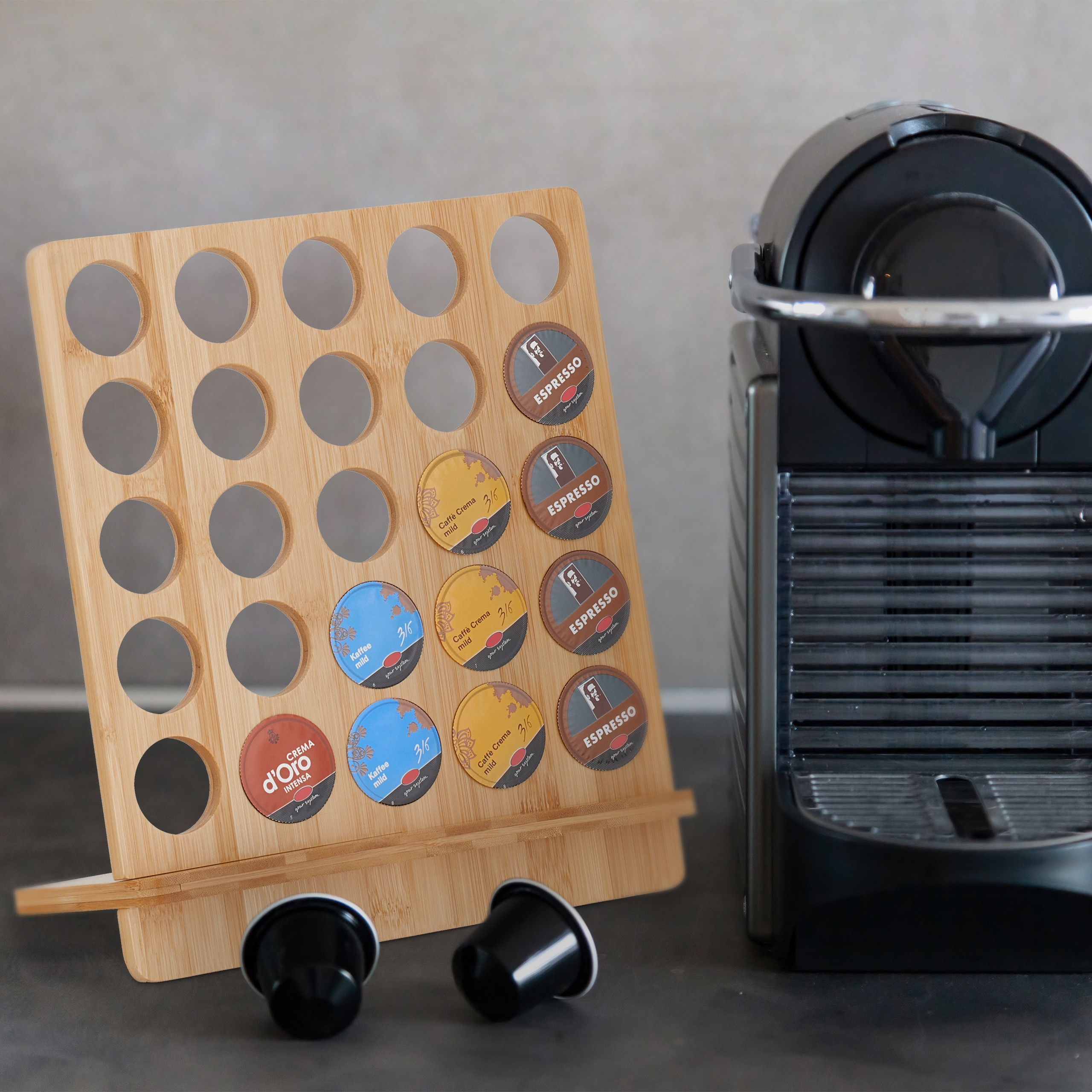 Ein hölzerner Kaffeekapselhalter steht auf einer Theke neben einer schwarzen Kaffeemaschine.