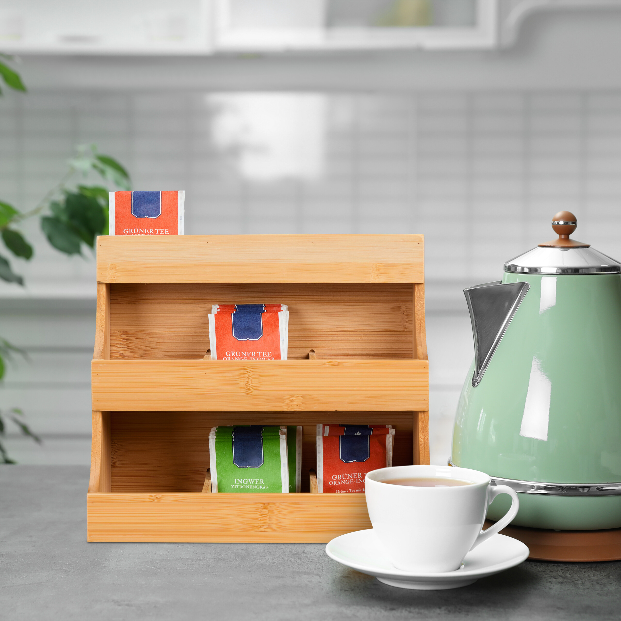 Holzregal mit Teebeuteln, daneben eine grüne Teekanne und eine weiße Tasse auf dem Tisch in einer Küche.