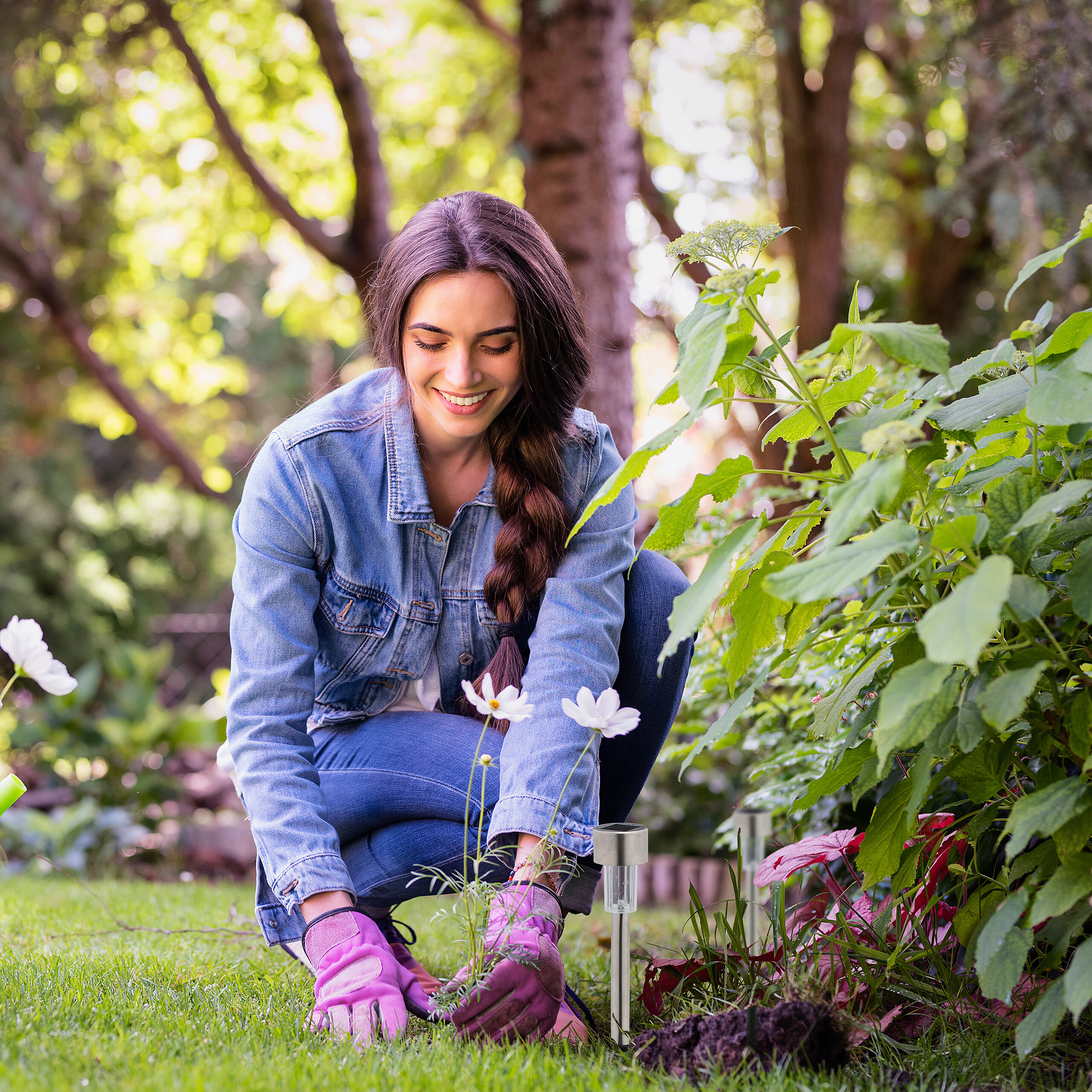 Eine lächelnde Frau kniet im Garten und pflegt grüne Pflanzen.