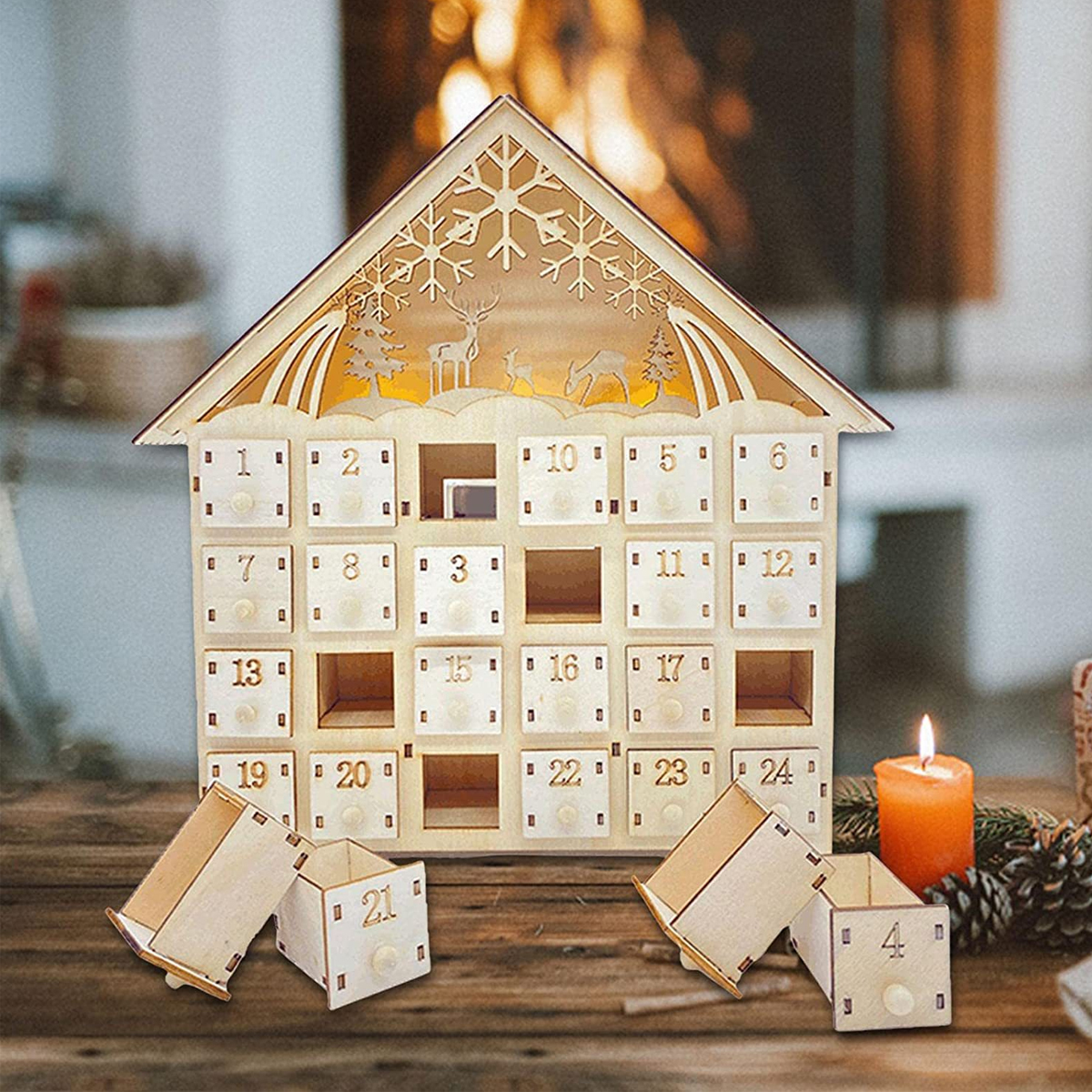 Ein hölzerner Adventskalender in Hausform mit nummerierten Schubladen, beleuchtetem Giebel und einer Kerze auf dem Tisch.