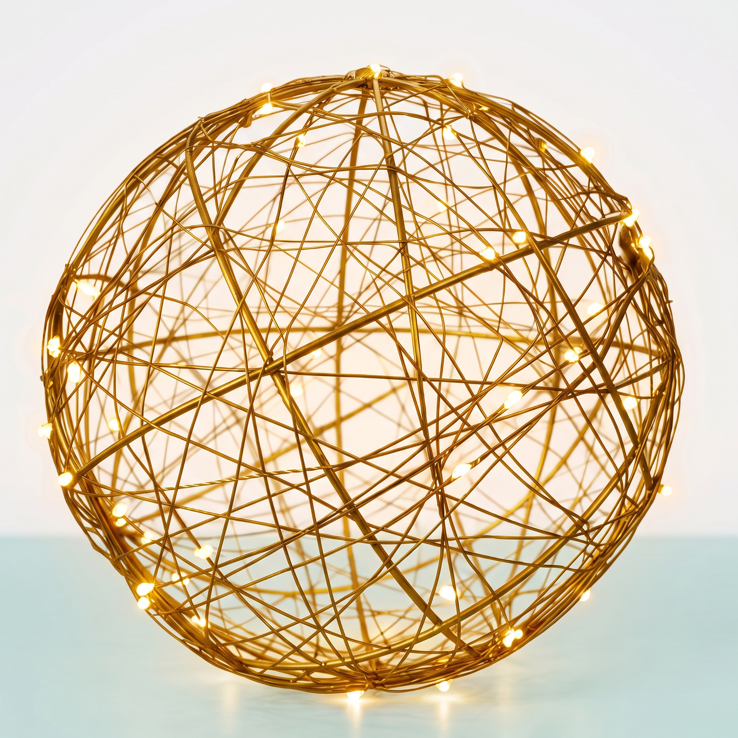 Eine dekorative goldene Drahtkugel mit kleinen Lichtern auf einem hellen Tisch.