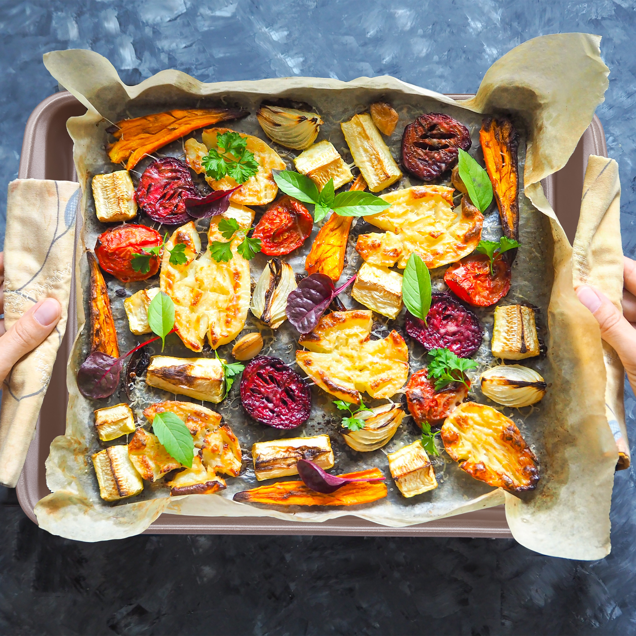 Ein Backblech mit verschiedenen gerösteten Gemüsesorten wie Tomaten, Karotten und Rote Bete, garniert mit Kräutern.