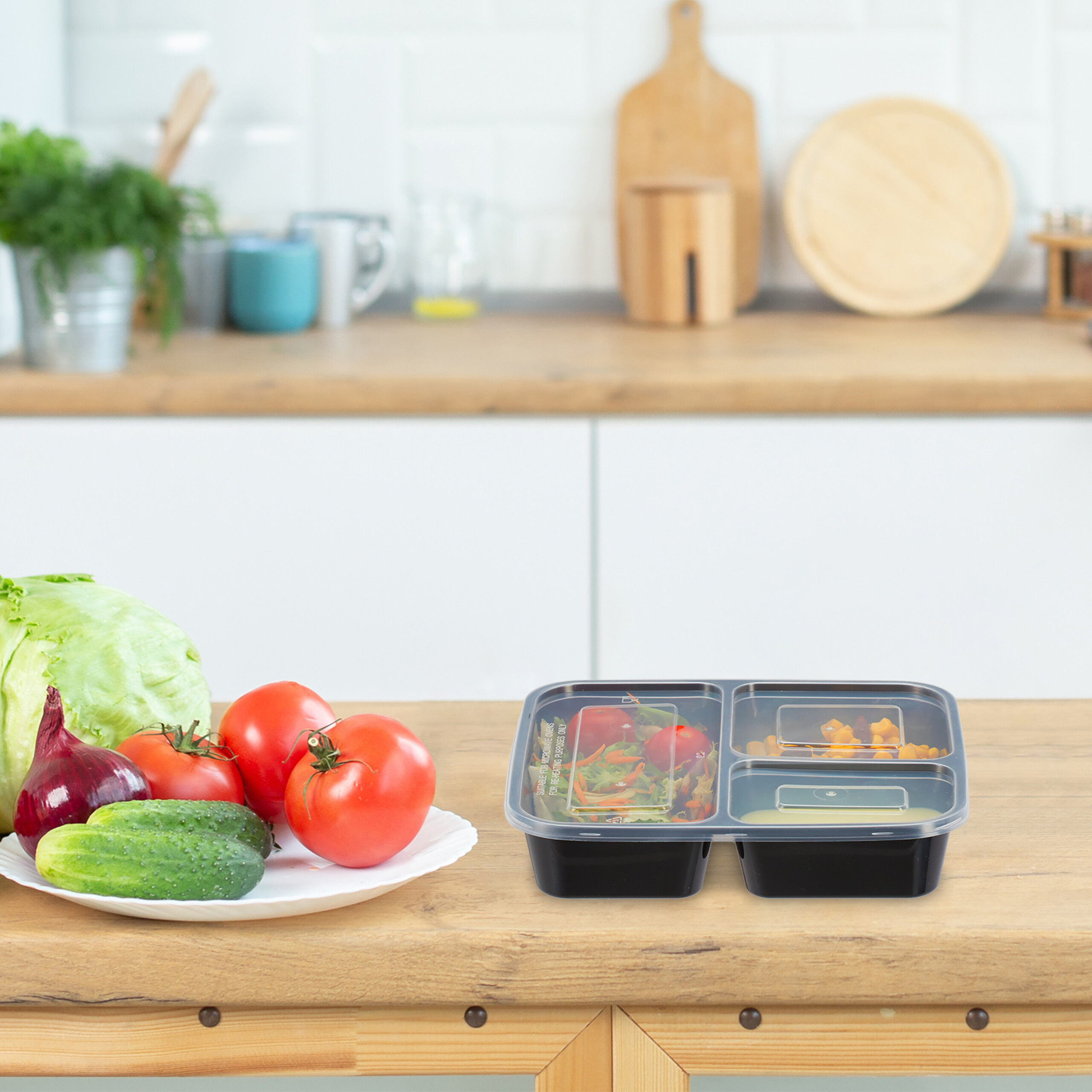 Ein Teller mit frischem Gem üse und ein Meal-Prep-Behälter auf einer Holztheke vor Küchenhintergrund.