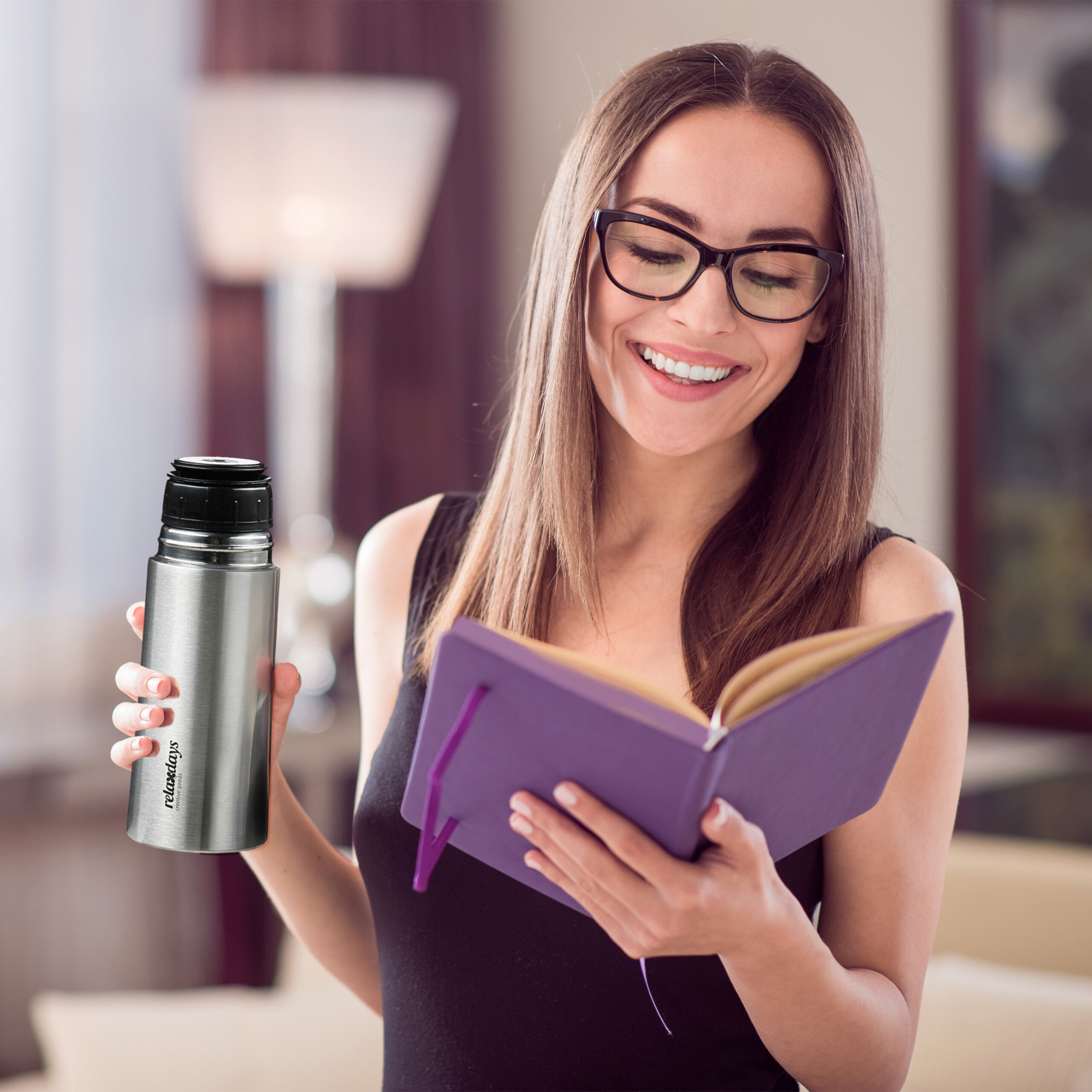 Lächelnte Frau in Brille liest ein violettes Notizbuch und hält eine Thermoskanne.