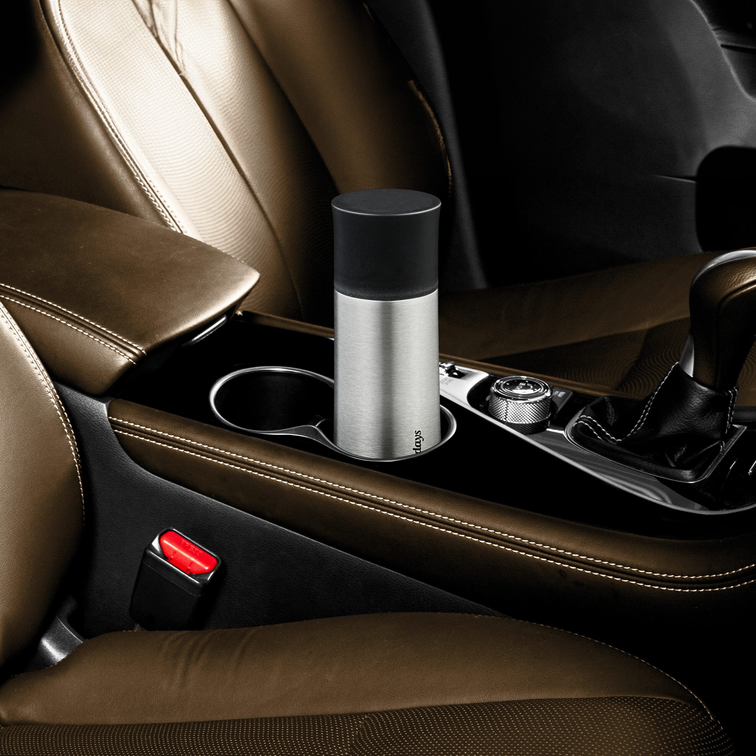 Ein silberner Thermobecher steht im Getränkehalter einer luxuriösen braunen Auto-Mittelkonsole.