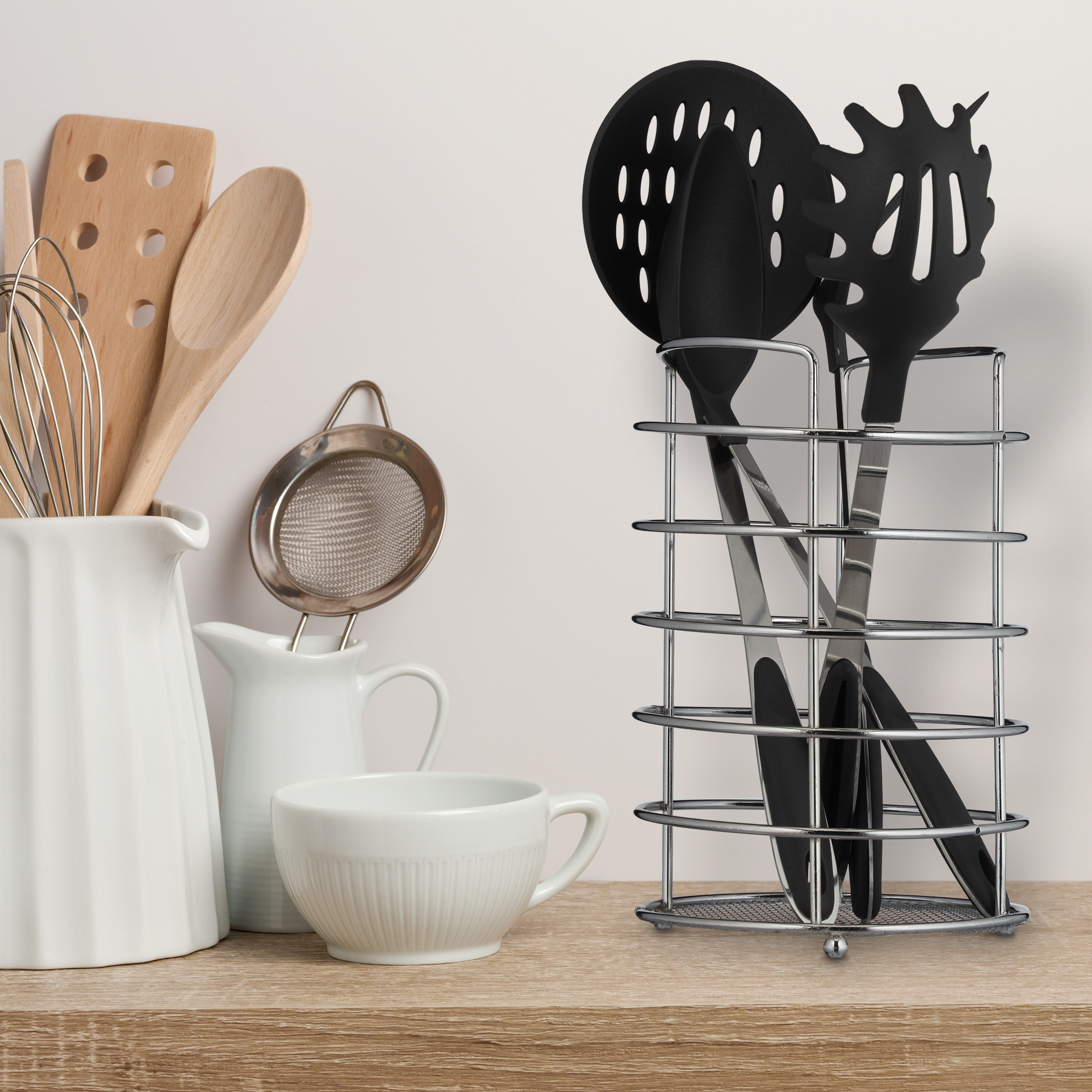 Küchenutensilien wie Holzlöffel in einer weißen Vase und schwarze Utensilien in einem Metallständer auf einem Regal.