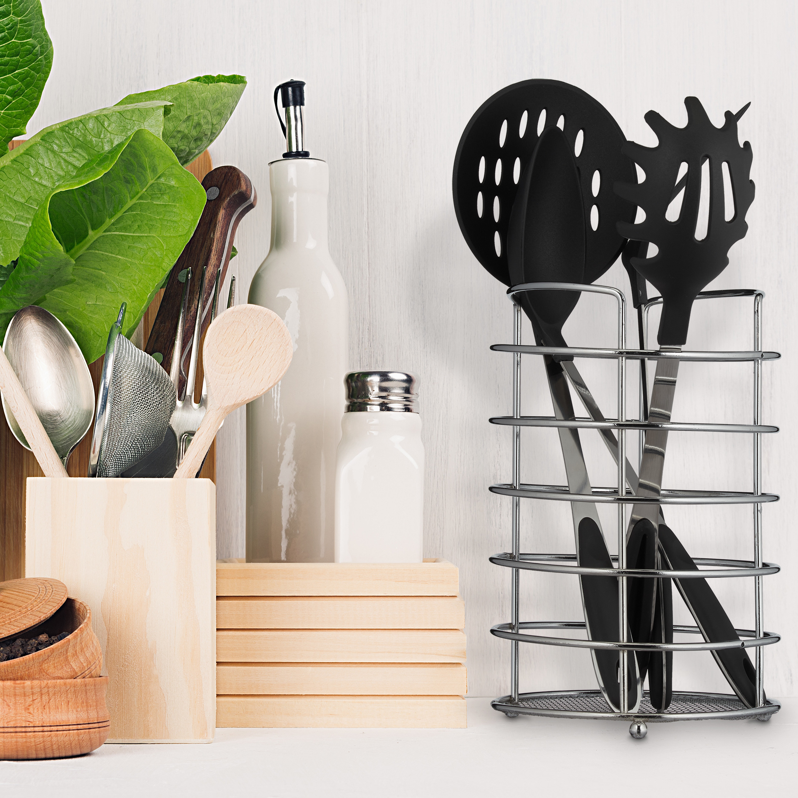 Küchenzeile mit Besteckhalter, grünen Blättern, weißer Ölflasche, Salzdose und Metallständer mit schwarzen Utensilien.