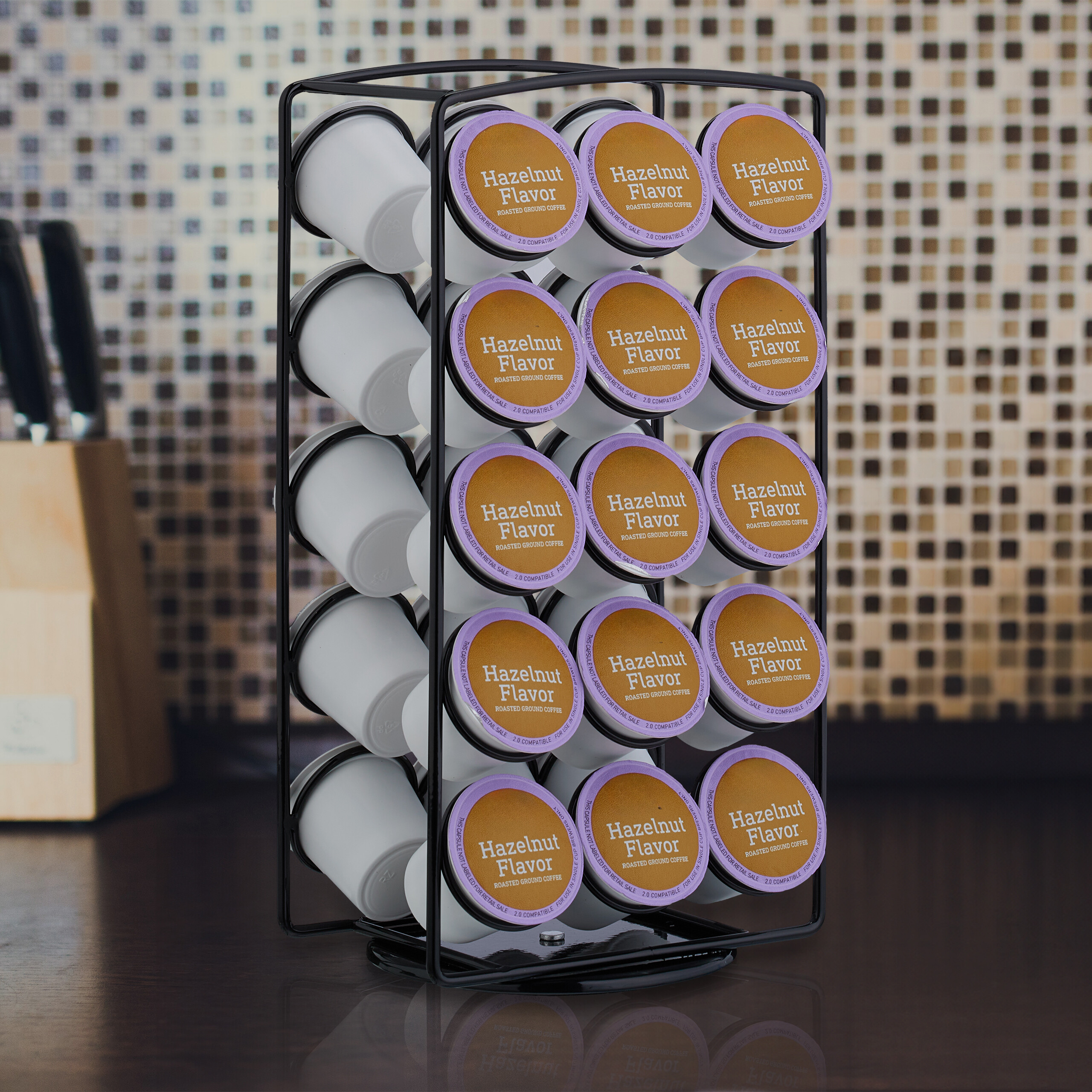 Ein schwarzer Drahtständer hält Reihen von Haselnuss-Kaffeepads in einer Küche mit gefliester Wand.
