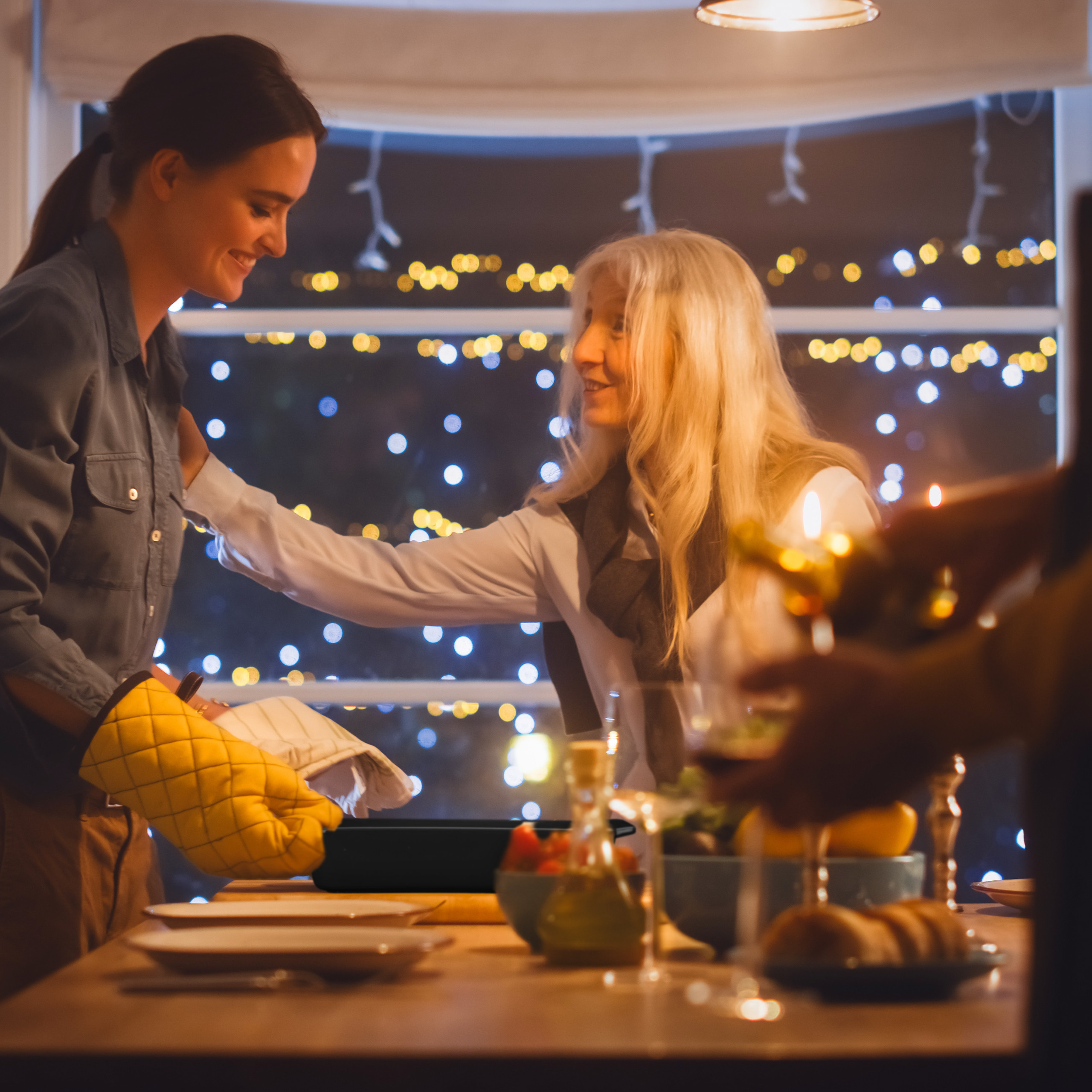Zwei Frauen stehen am gedeckten Tisch vor einem Fenster mit Lichterketten.