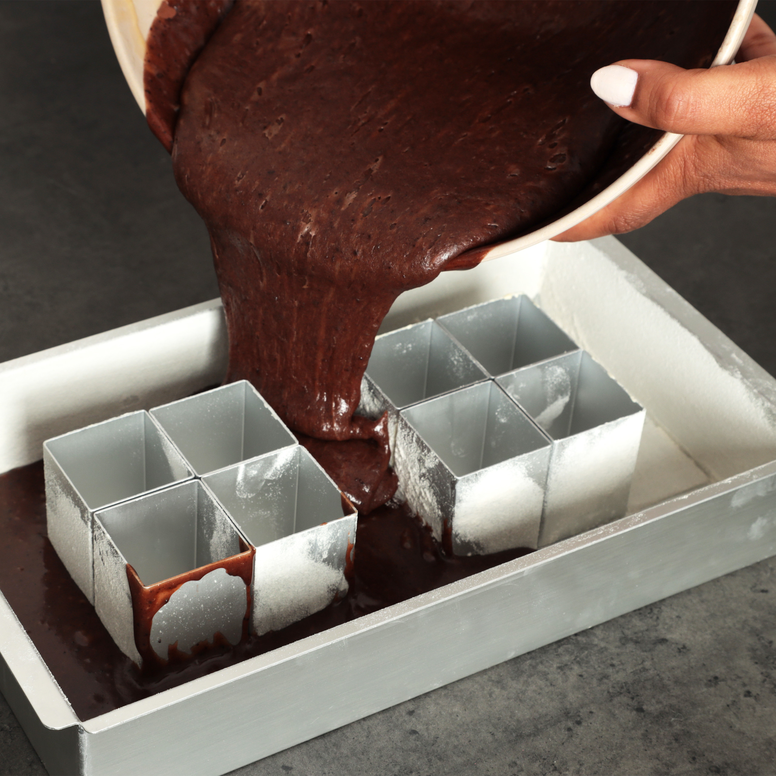 Dunklen Schokoladenteig aus einer Schüssel in quadratische Metallformen gießen.