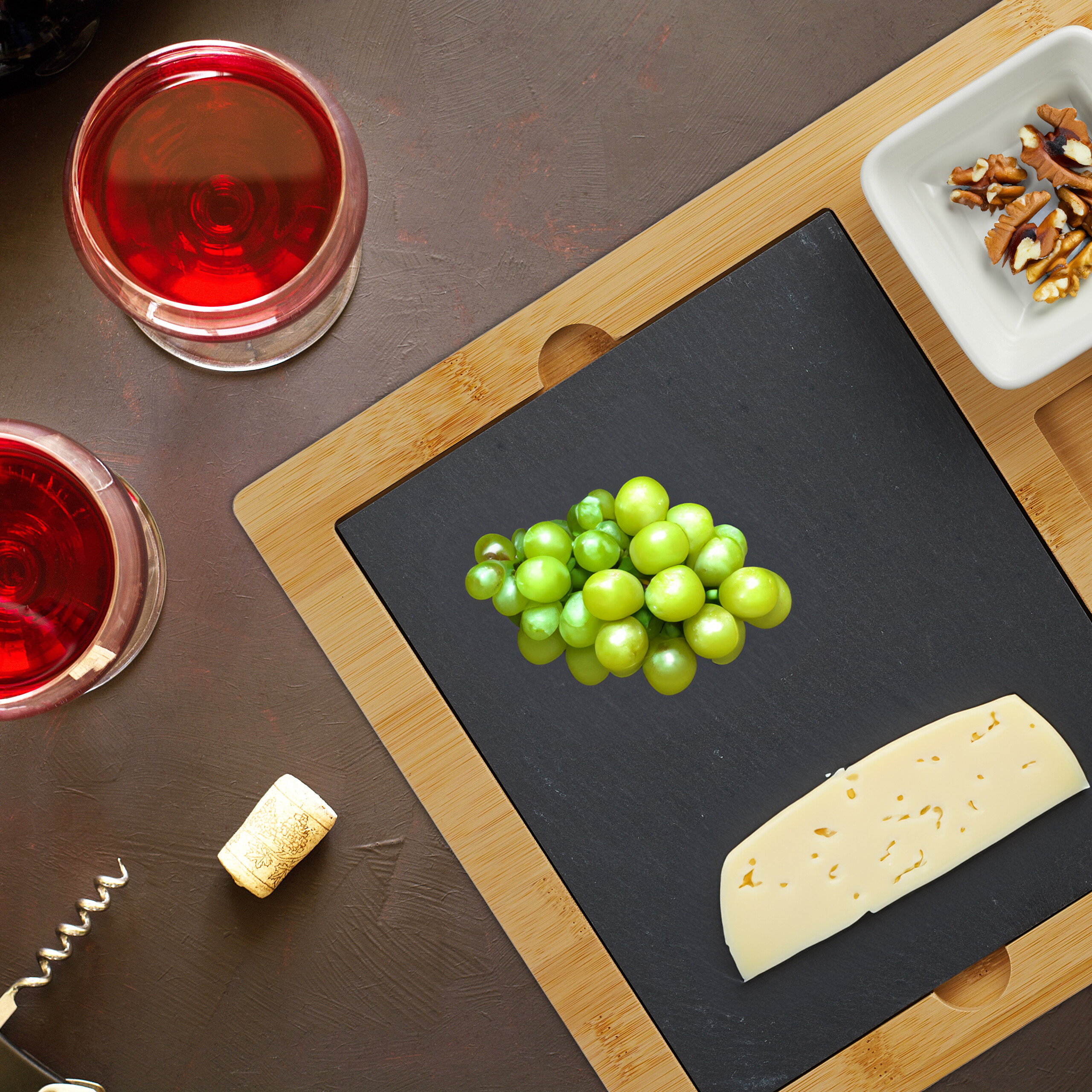 Rotwein, Trauben, Käse und Nüsse auf einem Holz- und Schieferbrett.