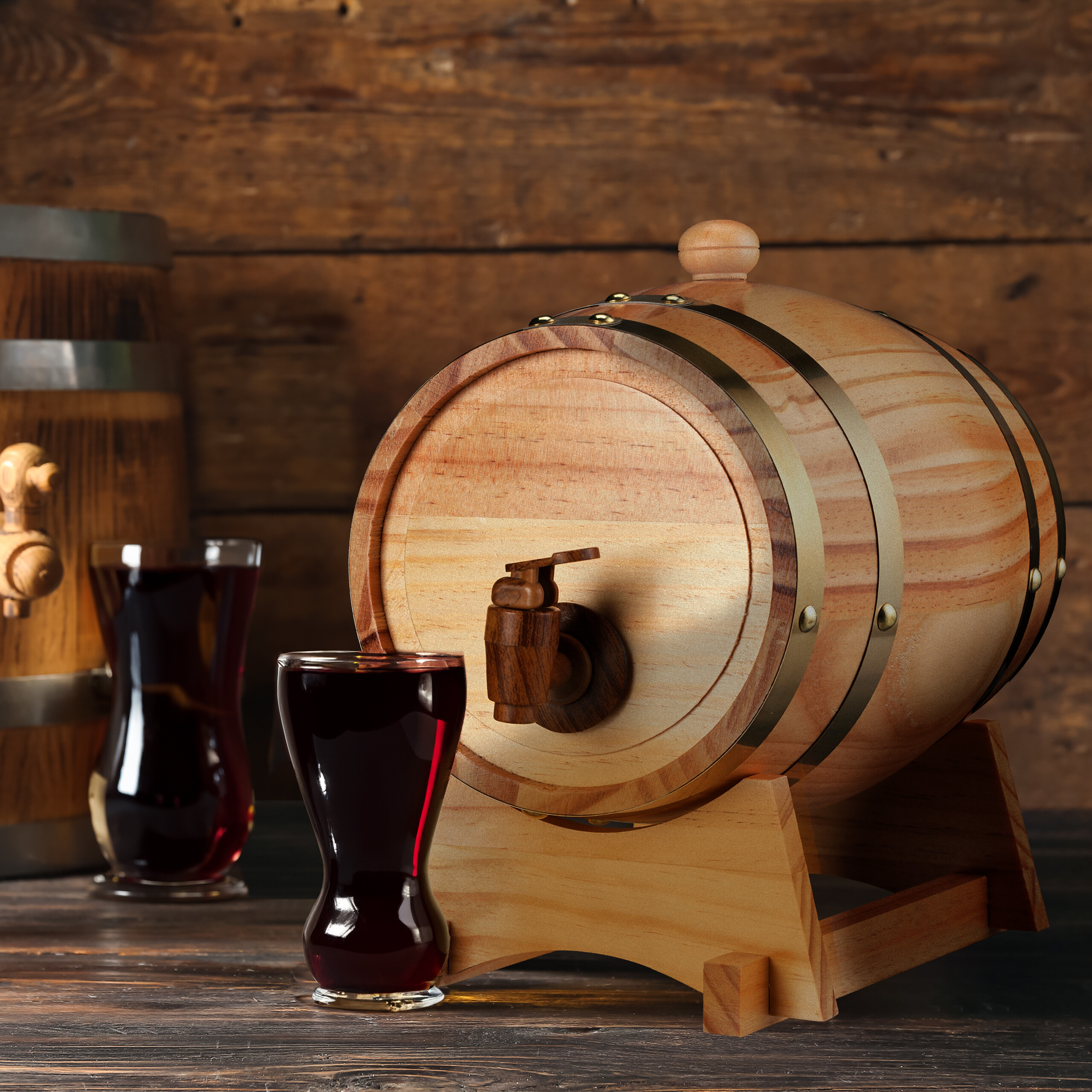 Ein Holzfass mit Hahn steht auf einem dunklen Tisch, neben einem Glas Rotwein, im Hintergrund ein weiteres Fass.