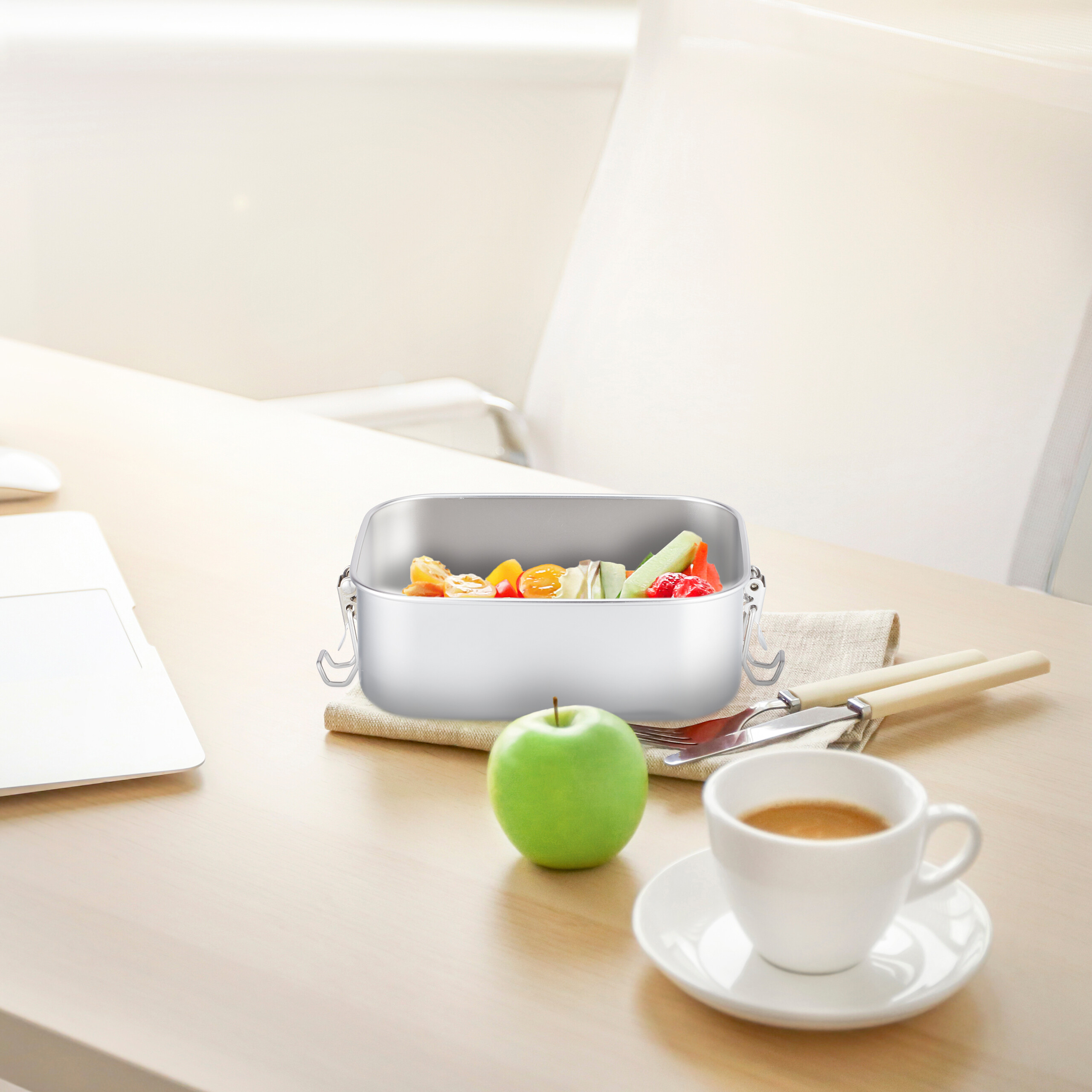 Eine Edelstahl-Lunchbox mit Gemüse auf einem Holztisch, daneben ein grüner Apfel und eine Kaffeetasse.