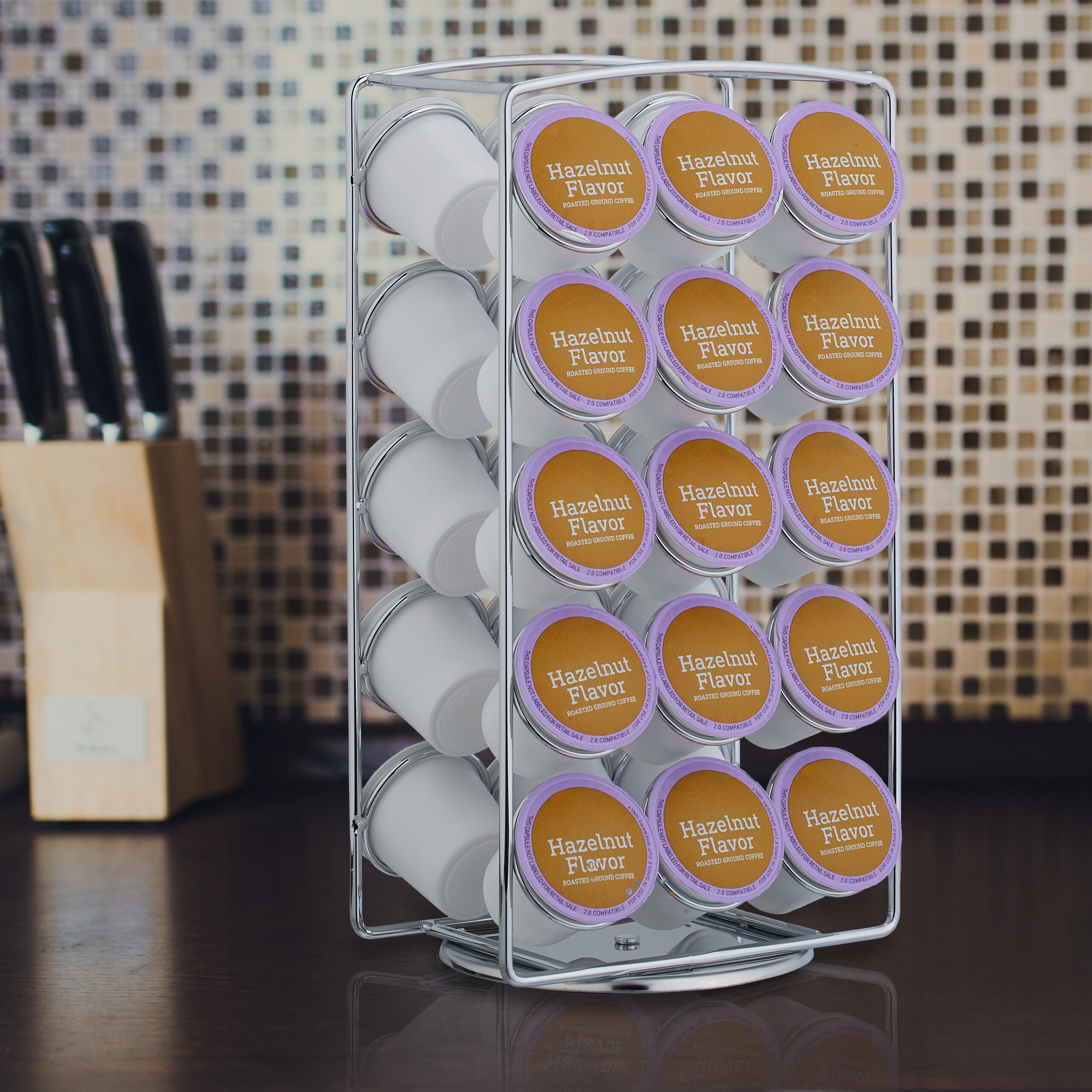 Ein Chrom-Karussell hält Haselnuss-Kaffeepads vor einer verschwommenen Küchenwand mit Messerblock.