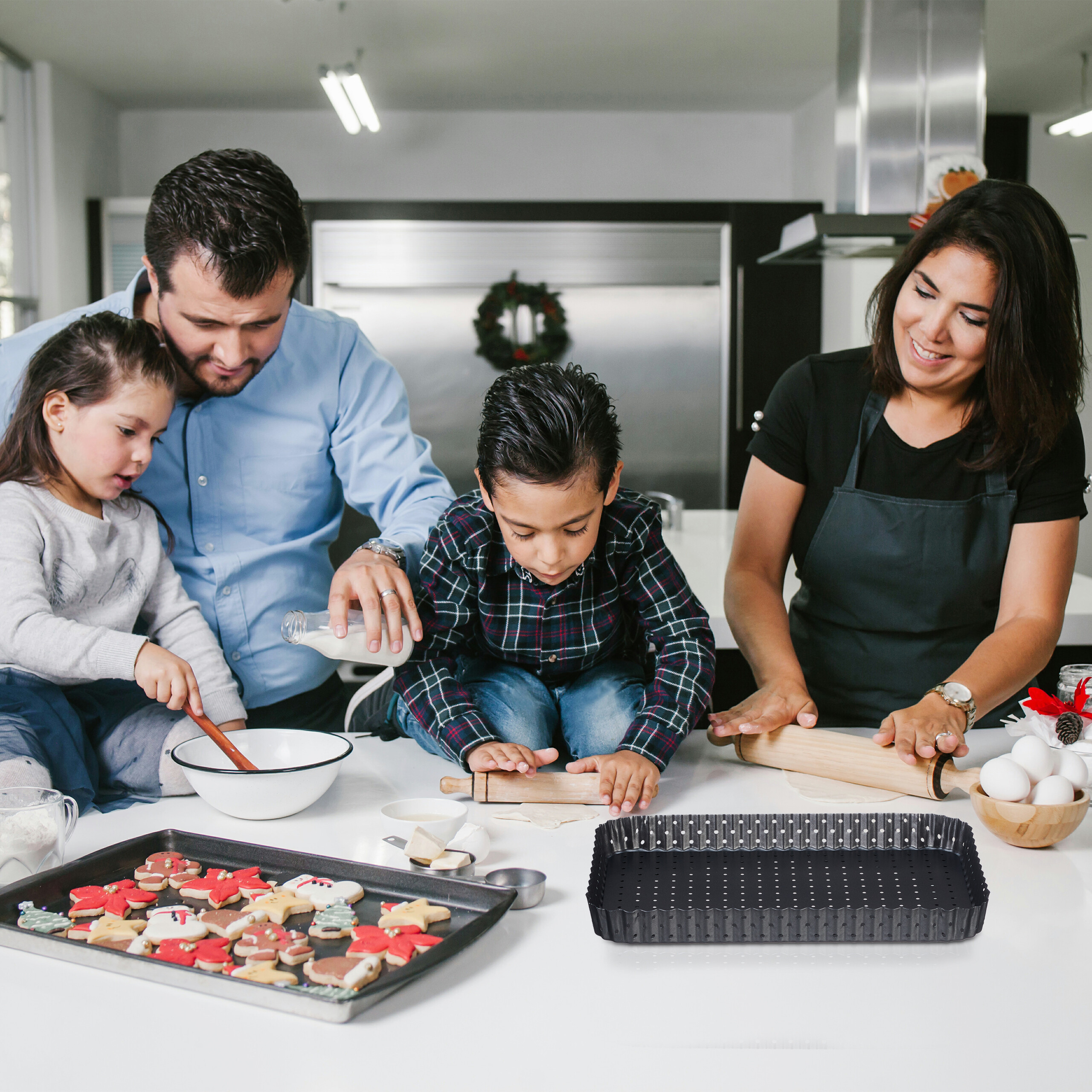 Eine vierköpfige Familie beim Weihnachtsplätzchenbacken in einer Küche, mit Plätzchen auf dem Blech und einer Tarteform.