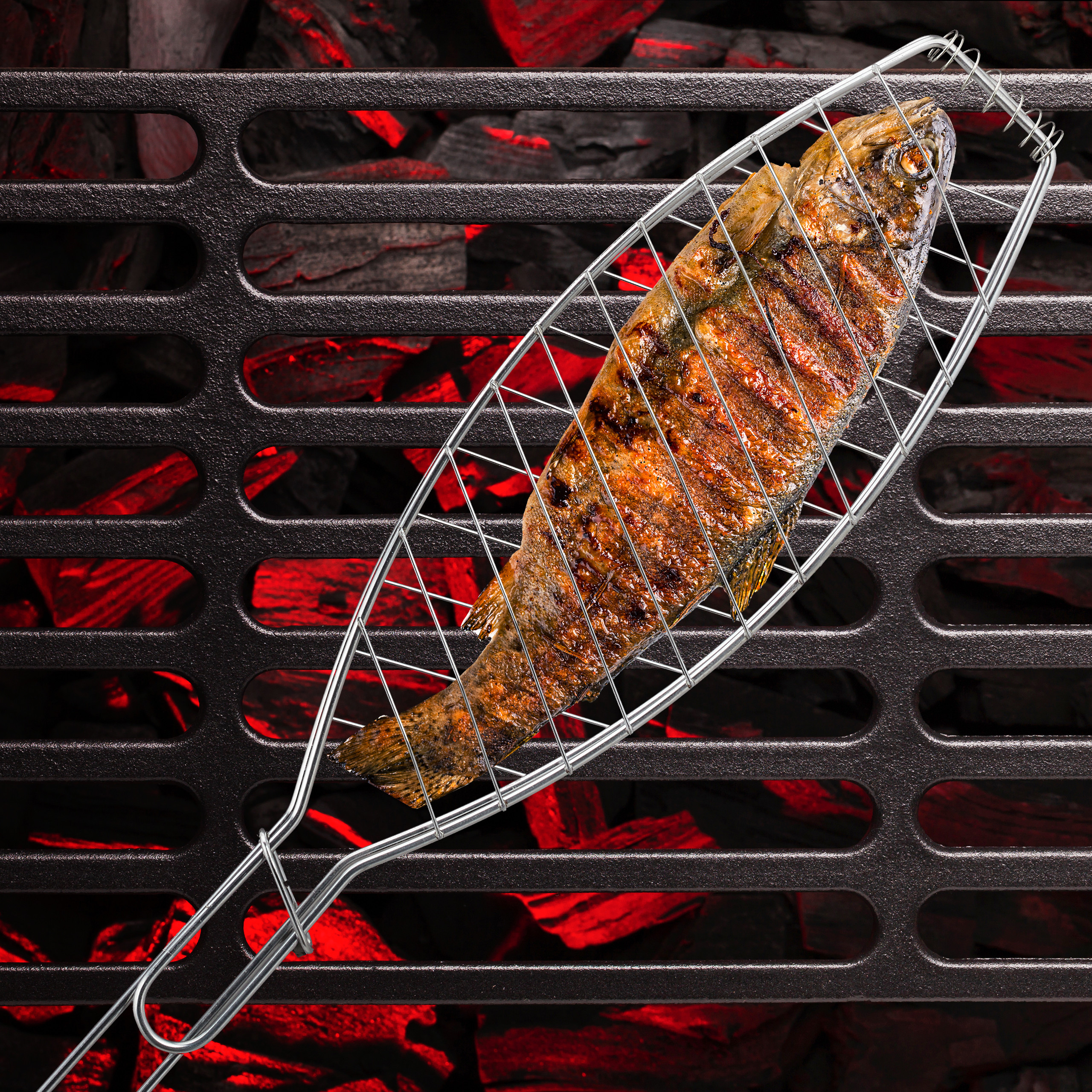 Ein ganzer Fisch liegt in einem Grillkorb auf einem Grillrost über glühender Kohle.