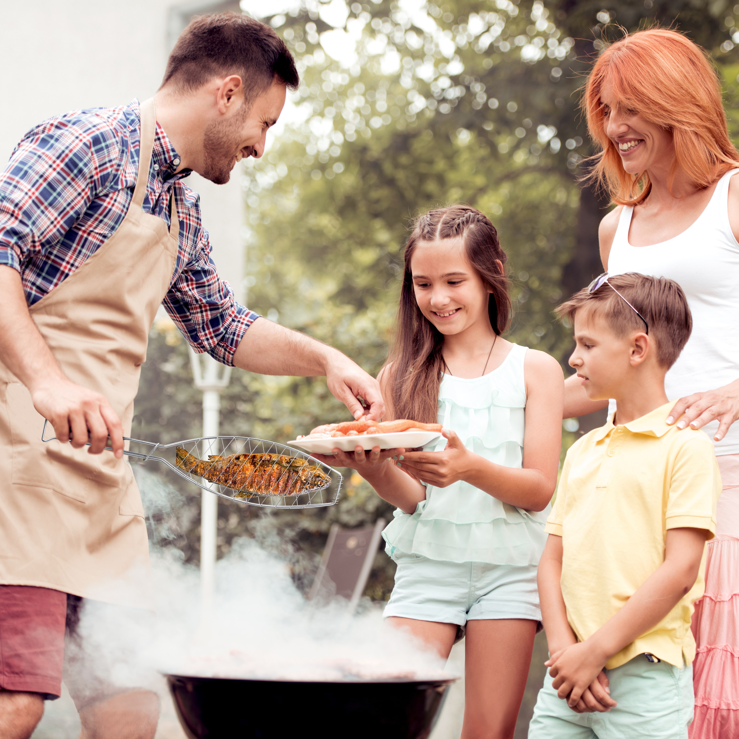 Eine Familie grillt im Garten. Der Vater grillt Fisch, während Kinder und Mutter zuschauen.