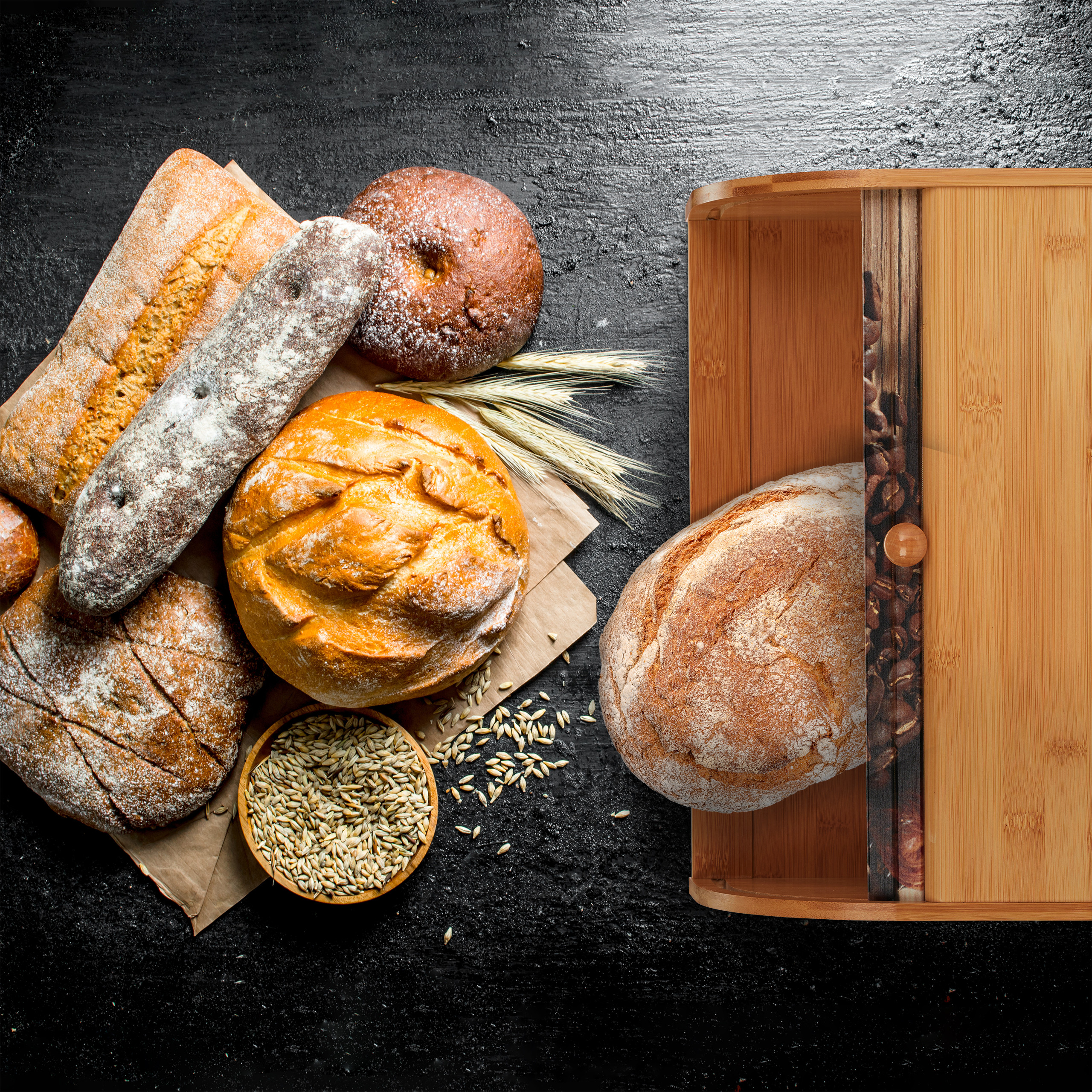 Verschiedene Brotsorten und Getreidekörner auf schwarzem Tisch, teils in einem Holzbrotkasten.