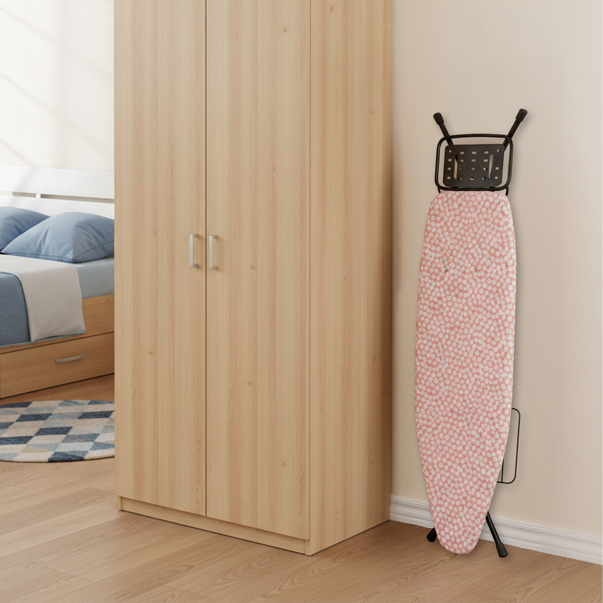 Ein faltbares Bügelbrett mit rosa Blumenbezug steht an der Wand neben einem hellen Holzschrank.