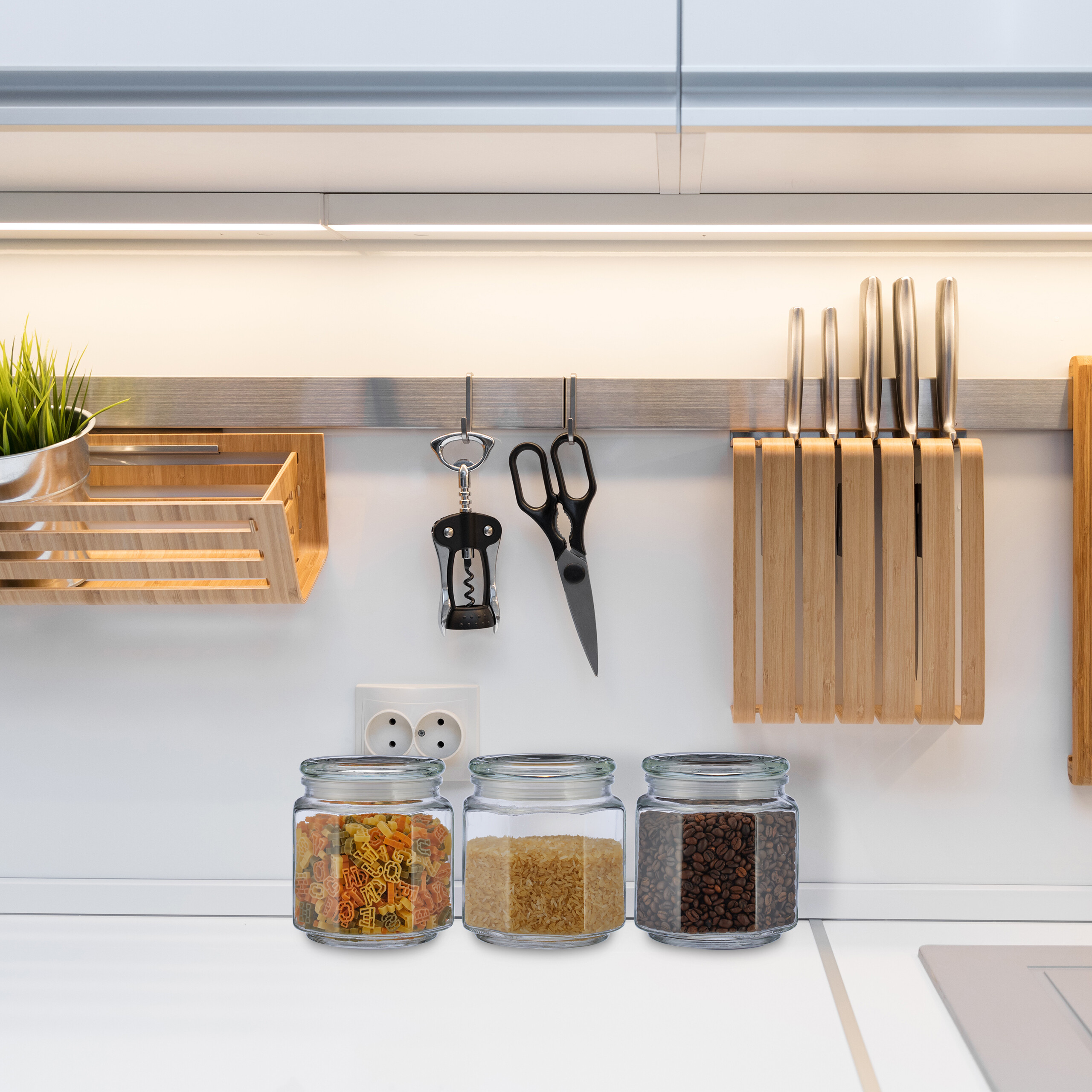 Moderne Küche mit Gläsern für Teigwaren, Reis und Bohnen, aufgehängten Küchenutensilien und einem Holzmesserblock.
