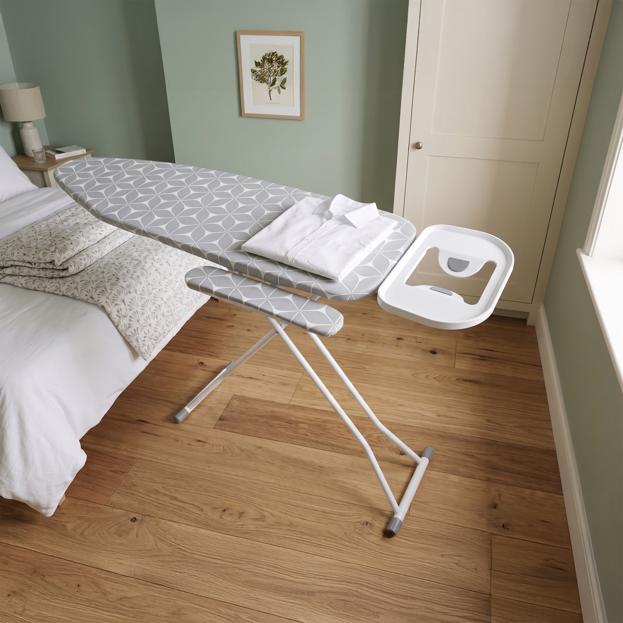 Ein graues Bügelbrett mit Muster steht in einem Schlafzimmer, darauf liegt ein weißes Hemd.