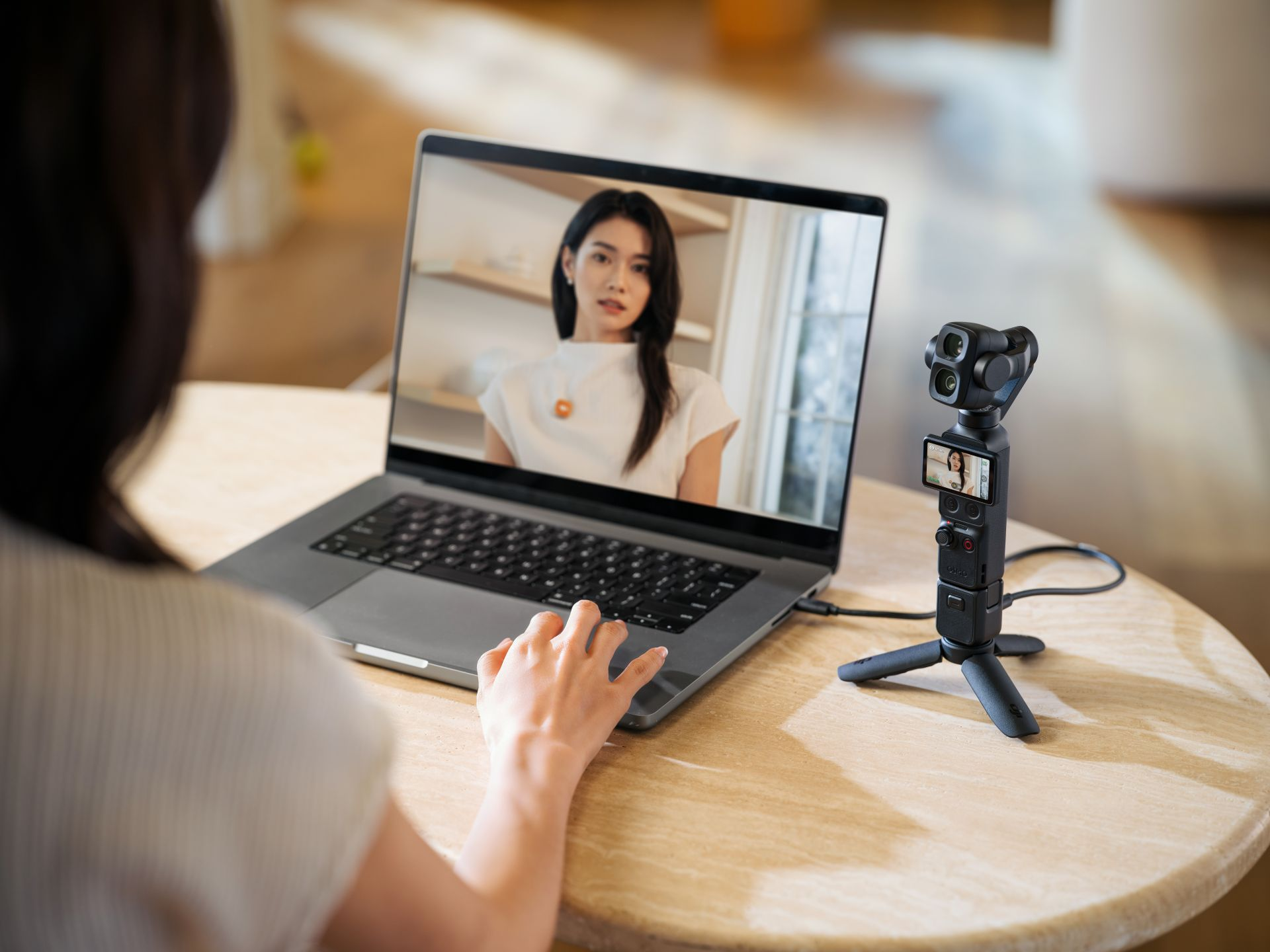 Bir kişi ahşap masada küçük bir tripod kamera yanında görüntülü arama açık dizüstü bilgisayar kullanıyor.