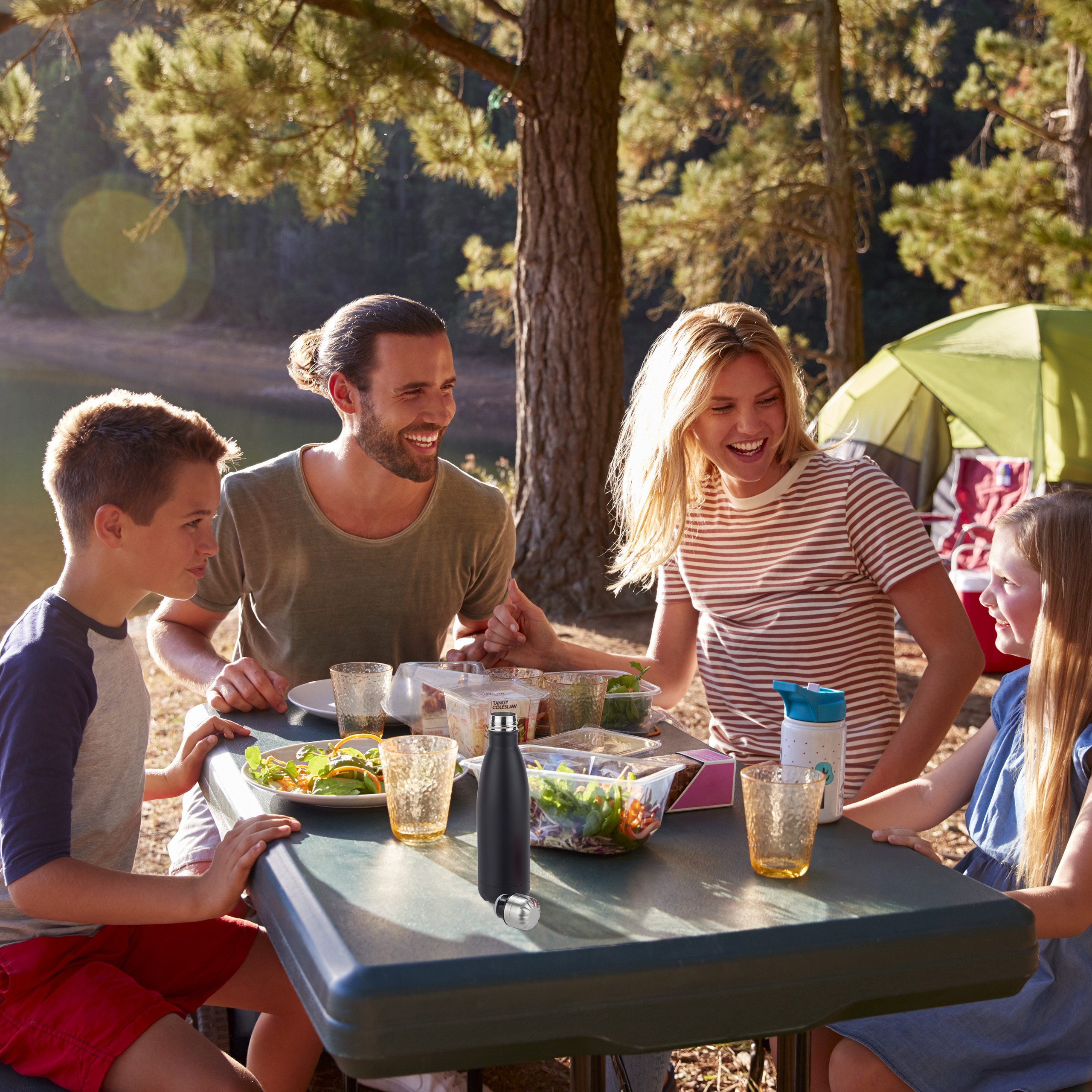 Eine Familie mit zwei Kindern beim Picknick im Wald an einem Tisch.