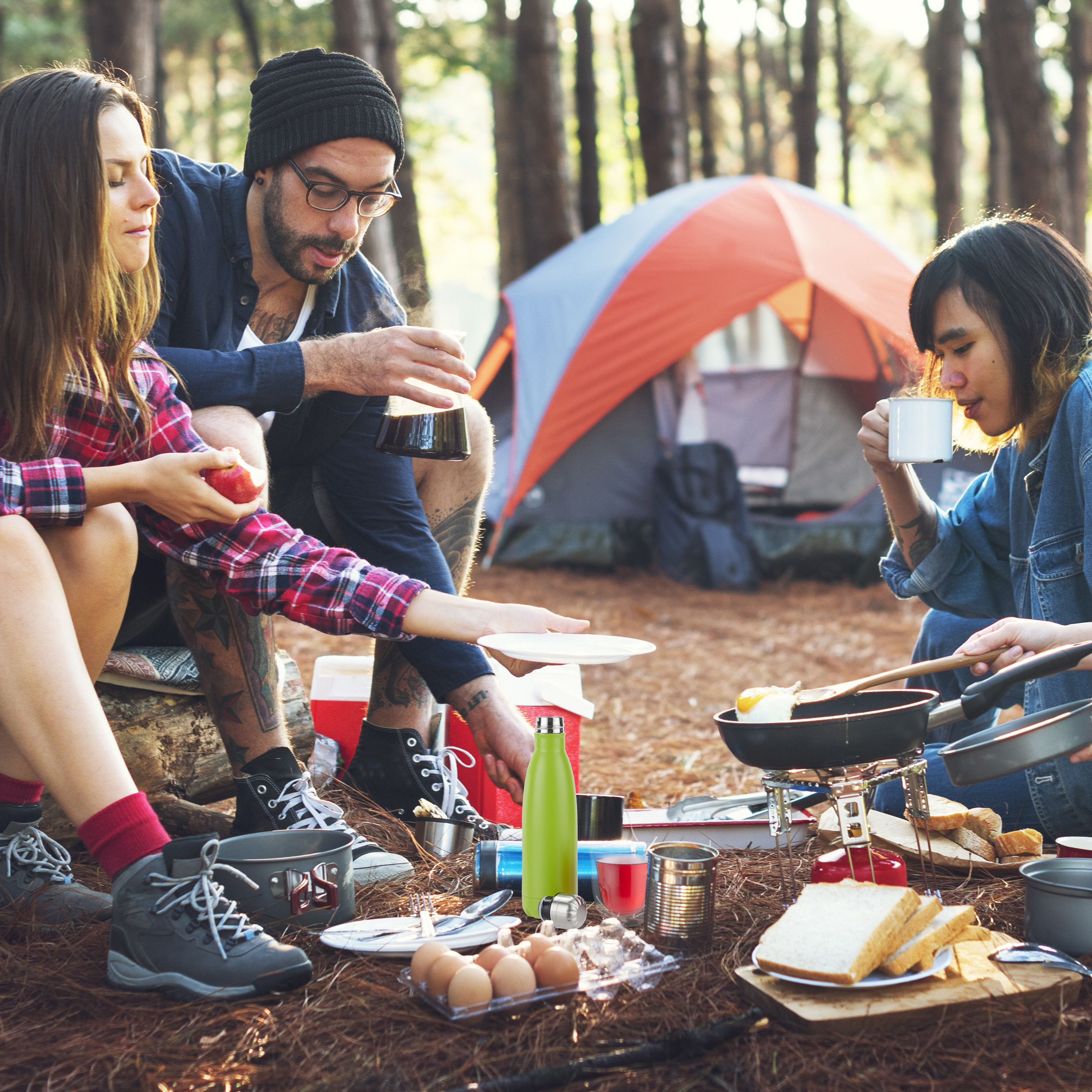 Drei Freunde campen im Wald, kochen nahe einem Zelt mit Brot, Eiern und Kaffee.