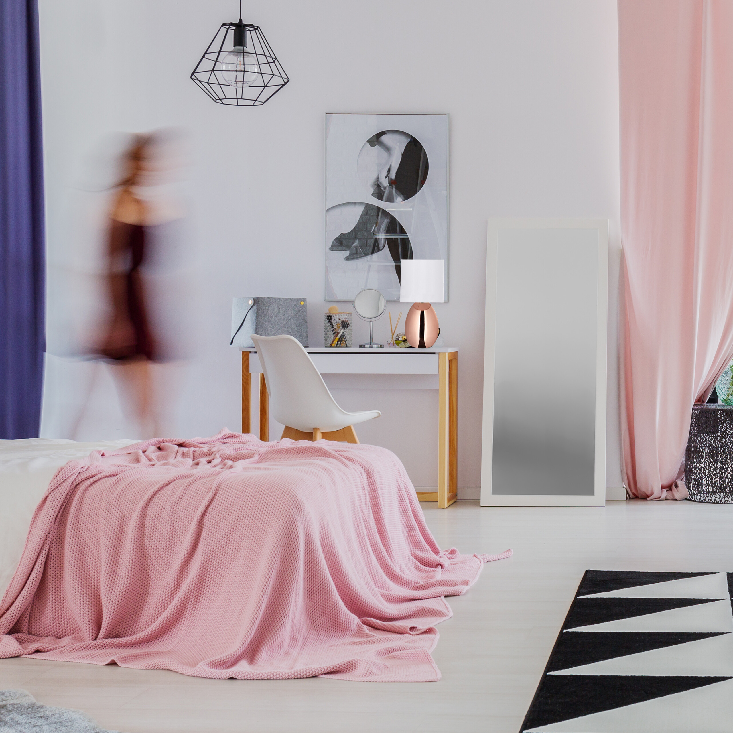 Modisches Schlafzimmer mit rosa Decke, weißem Schreibtisch und verschwommener Person.