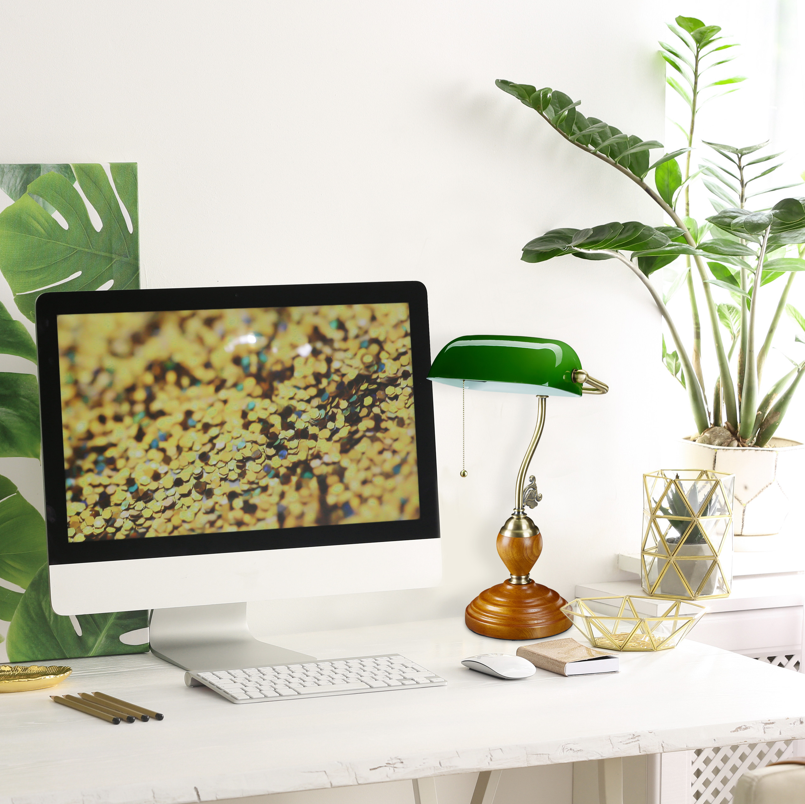 Ein weißer Schreibtisch mit einem Computer, einer grünen Lampe, goldenen Dekorationen und einer Topfpflanze.