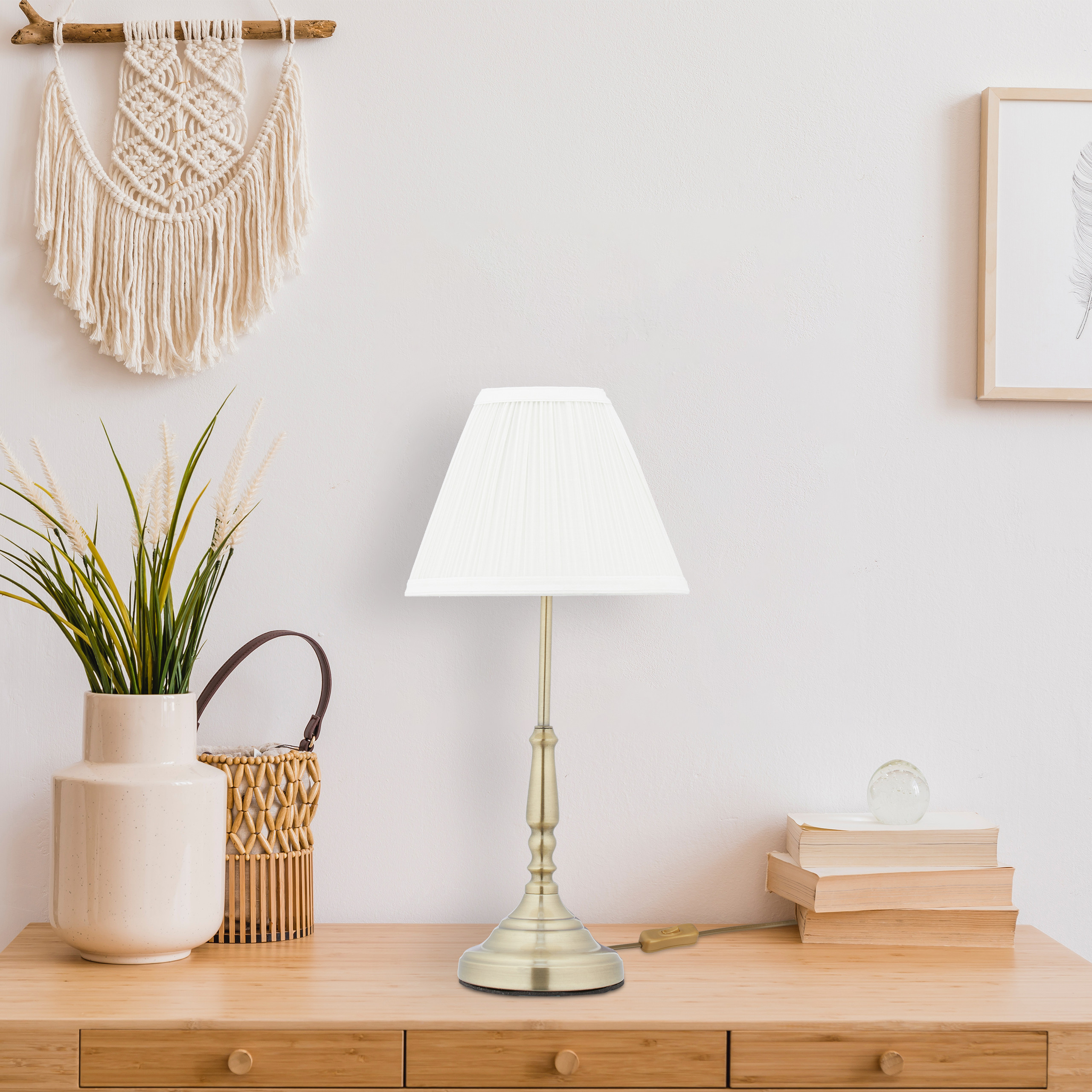 Ein weißer Lampenschirm auf einer Messinglampe steht auf einem Holztisch neben einer Blumenvase und Büchern.